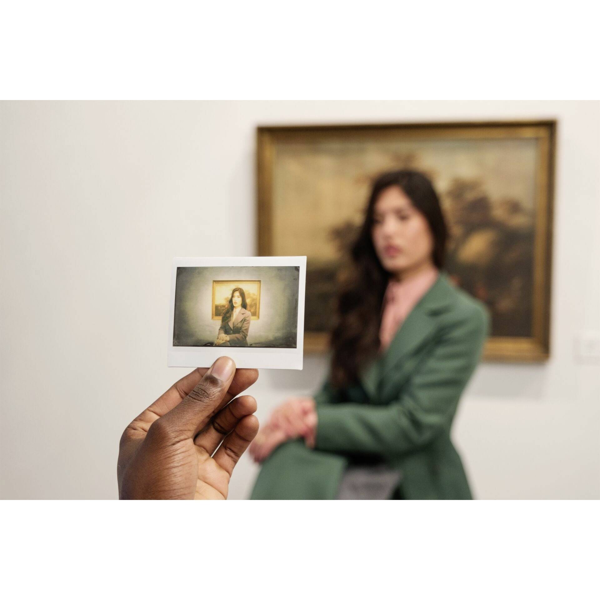 Rozmazaná žena sedí v galerii před obrazem. V ruce drží fotografii, která zobrazuje ostrou verzi téže ženy.