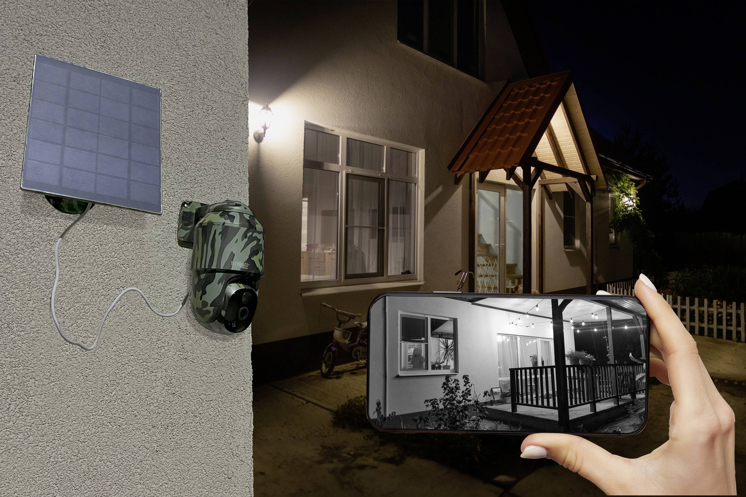 Bezpečnostní kamera na zdi domu, připojená k solárnímu panelu. Ruka drží smartphone zobrazující živý obraz.
