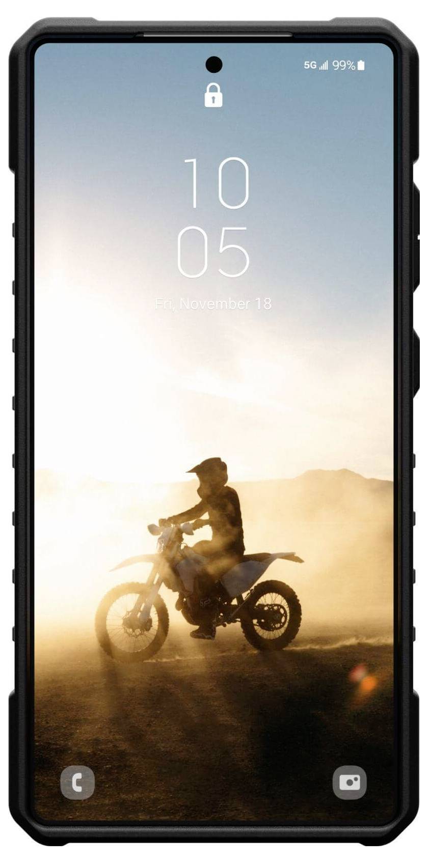 Displej smartphonu zobrazuje pozadí: Osoba jede na motocyklu v prašné krajině při západu slunce.