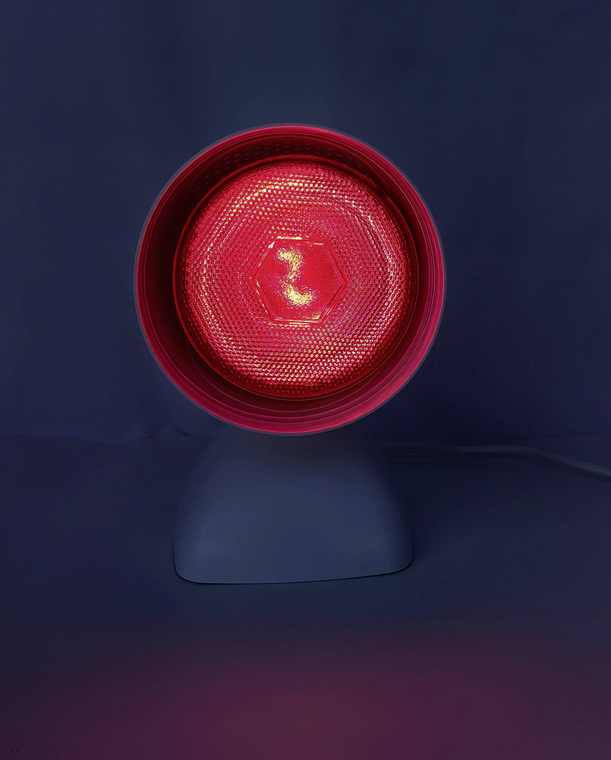 Červená infračervená lampa s kruhovým designem na tmavém pozadí, vyzařující teplé světlo, běžně používaná pro terapeutické účely.