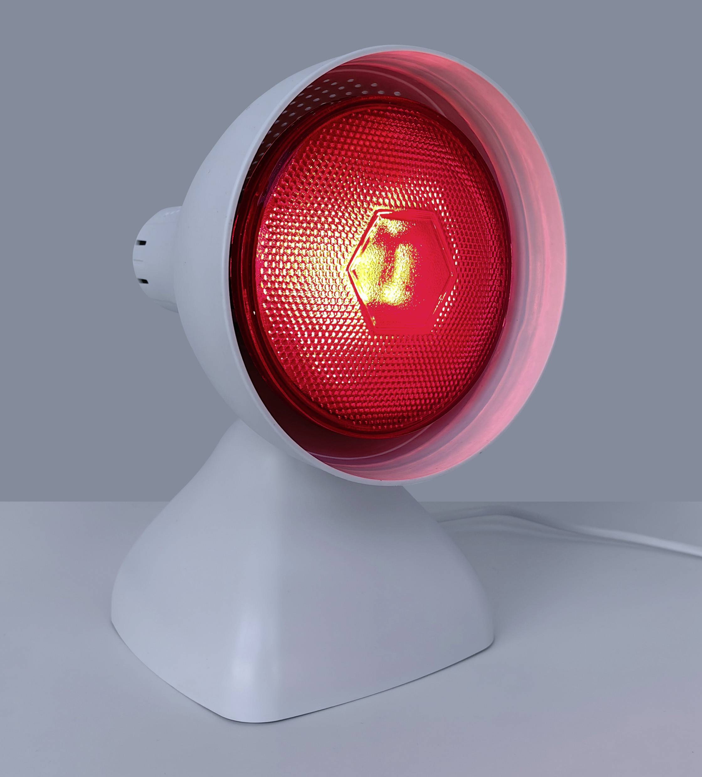 Bílá infračervená tepelná lampa s červeně světélkujícím světlem, umístěná na šedém povrchu, určená pro terapeutické účely.