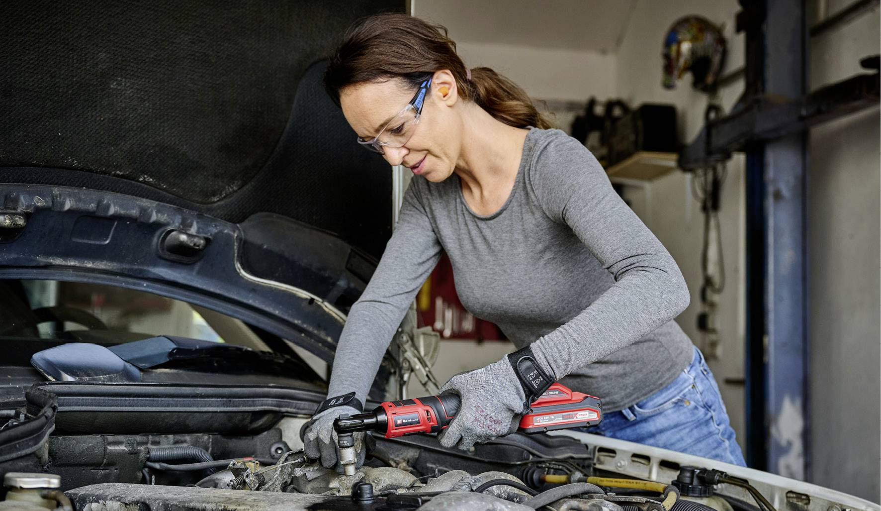 Žena opravuje autoplášť v autoservisu. Má na sobě ochranné brýle a rukavice a používá nářadí.