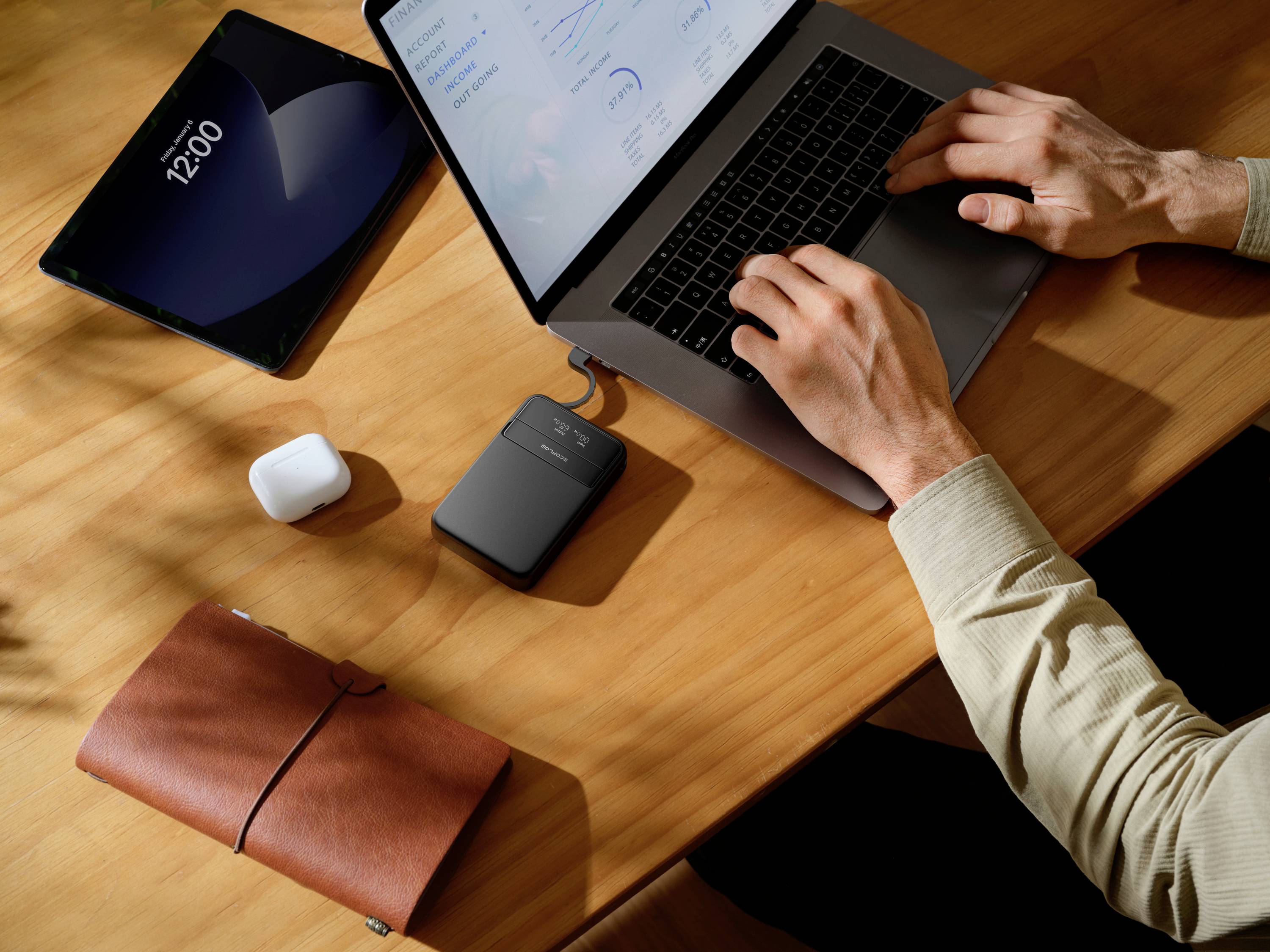 Osoba pracuje na laptopi u stolu. Vedle leží tablet, bezdrátová sluchátka, poznámkový blok a externí disk.