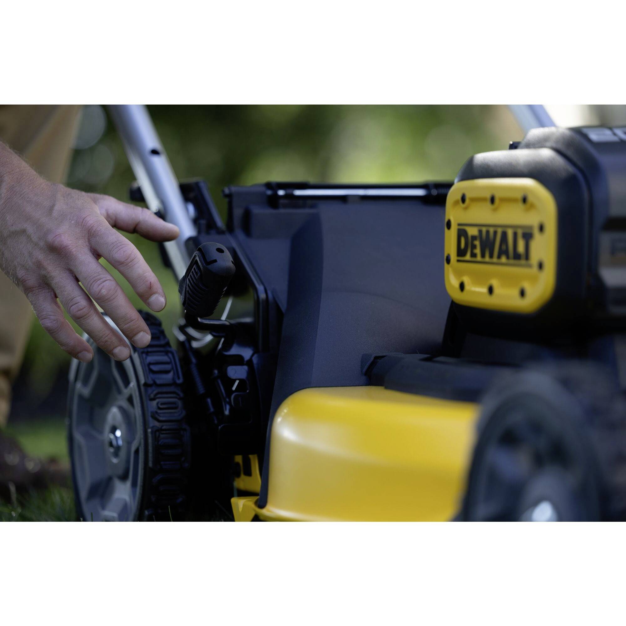 Sekačka značky DeWalt s viditelnou rukojetí a koly. Ruka se přibližuje k zařízení pro ovládání na zelené trávě.
