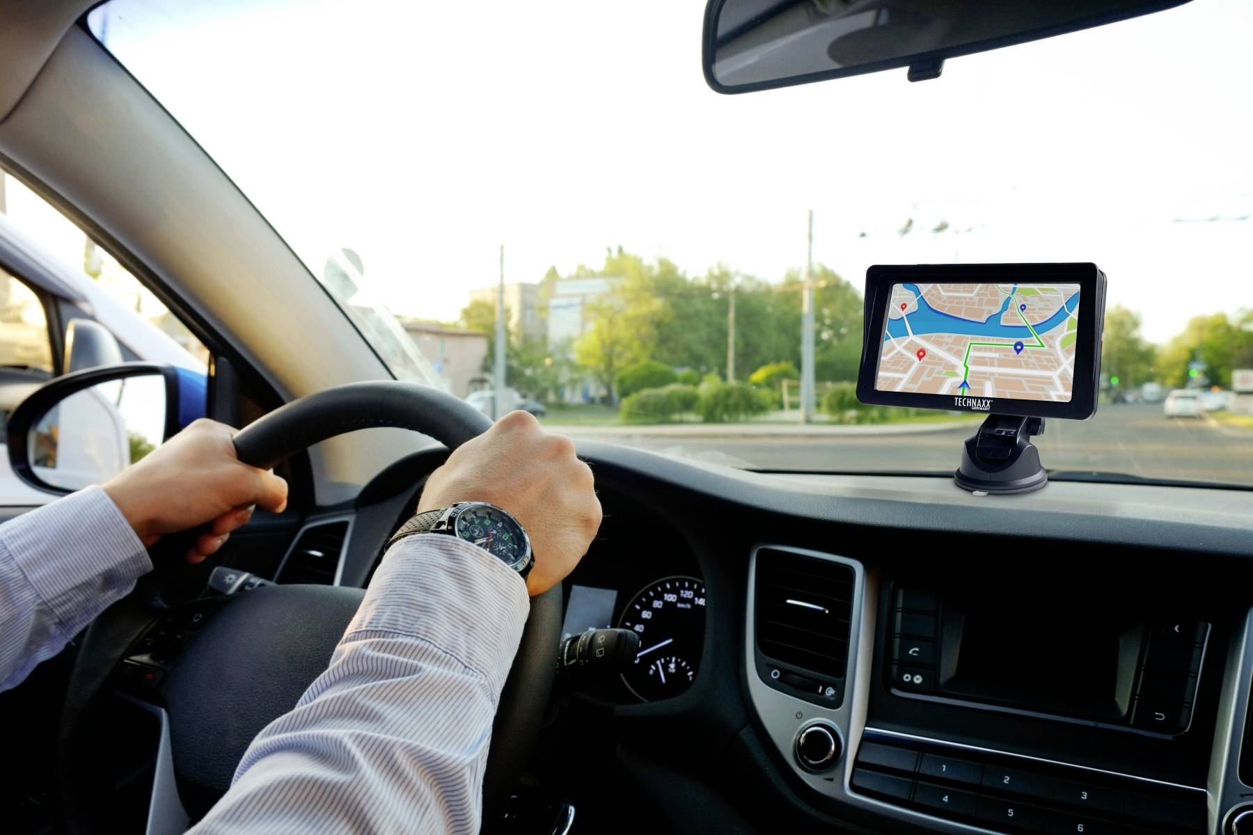 Osoba řídí automobil a dívá se na navigační zařízení, které zobrazuje městskou ulici jako trasu.