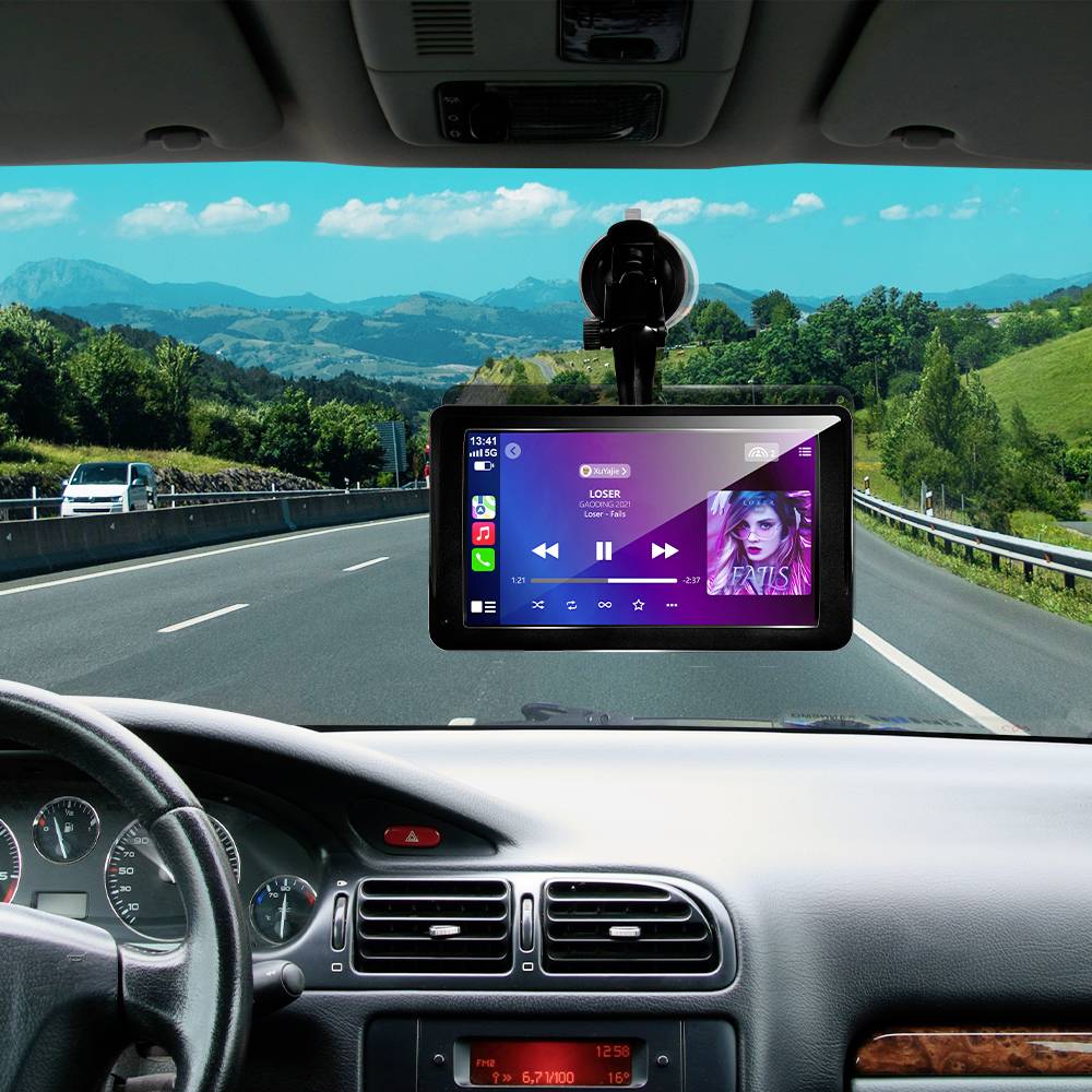 Jízda autem po venkovské silnici; navigační přístroj zobrazuje hudební přehrávač. V pozadí zelené zarostlé kopce.