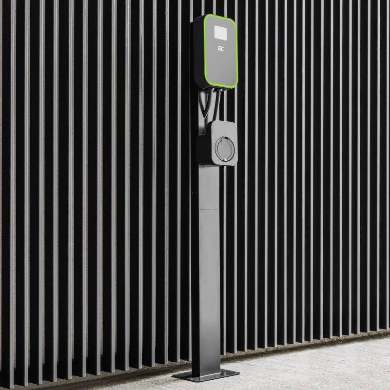 Černá nabíjecí stanice pro elektromobily před pruhovanou stěnou, s zeleným obrysem kolem displeje.