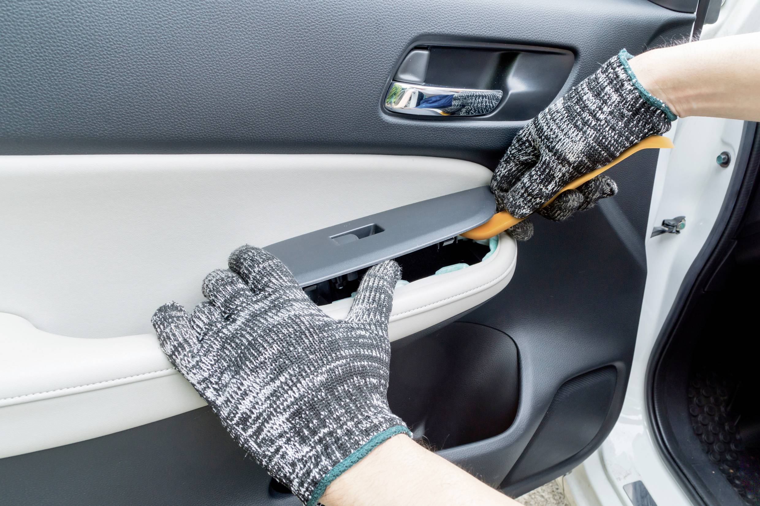 Dvě rukavicemi opatřené ruce odstraňují kryt kliky automobilu pomocí nástroje.