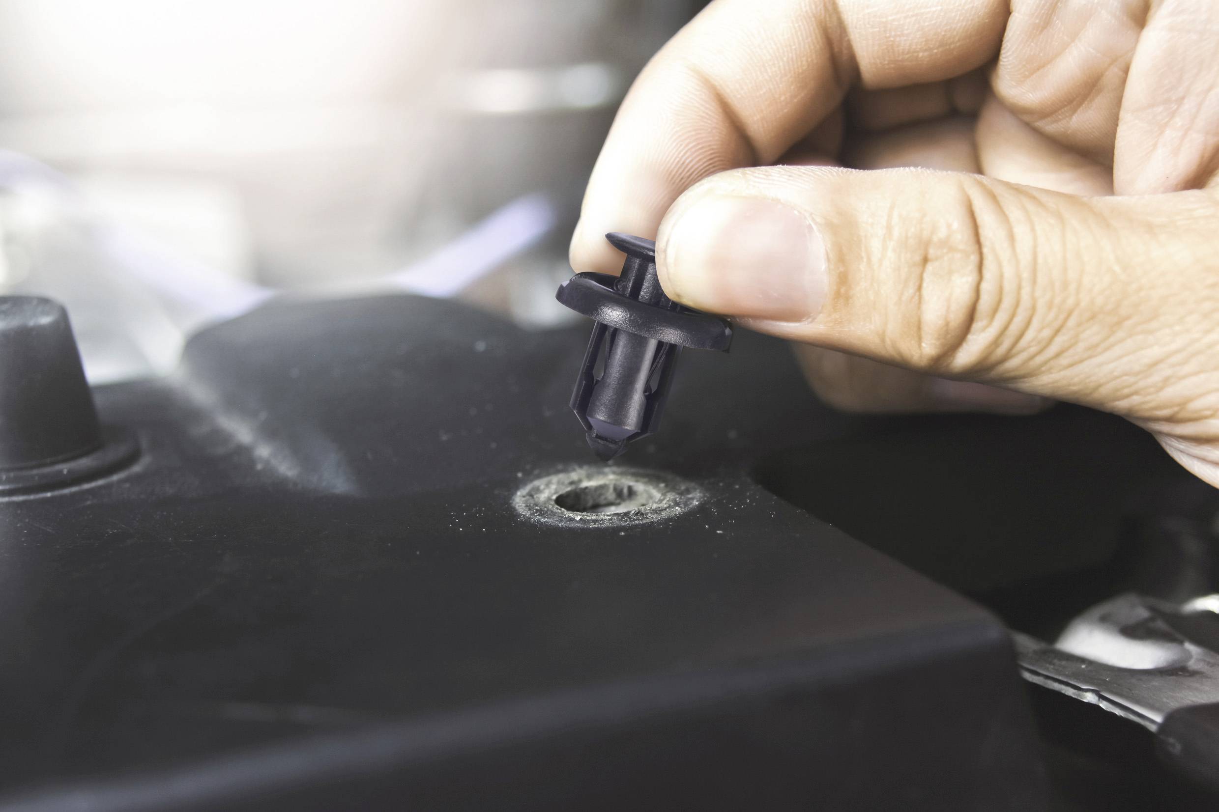 Ruka vkládá plastickou upevňovací sponu do otvoru černého dílu automobilu.