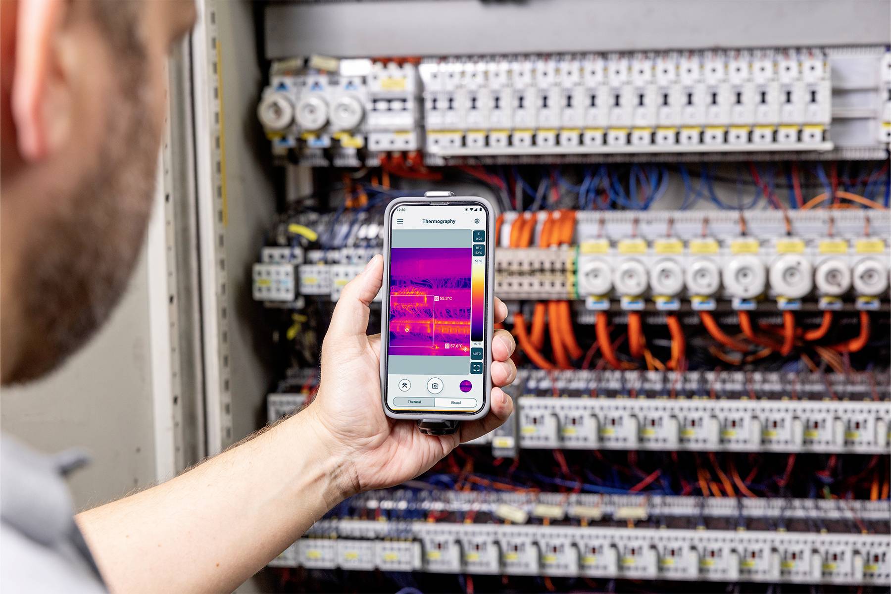 Osoba drží smartphone s funkcí termokamery před rozvaděčem. Na obrazovce jsou patrné teplotní rozdíly.