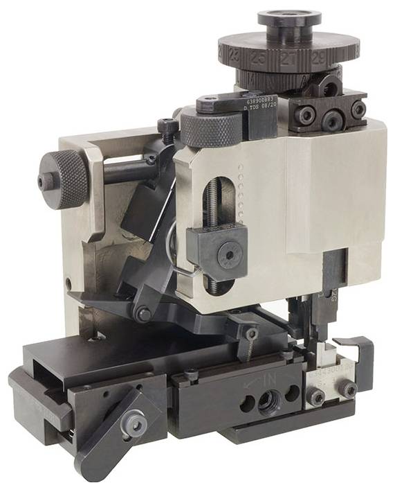 Strojní díl z kovu s několika ozubenými koly a otočnými knoflíky; vypadá jako mechanická komponenta nebo nástroj.