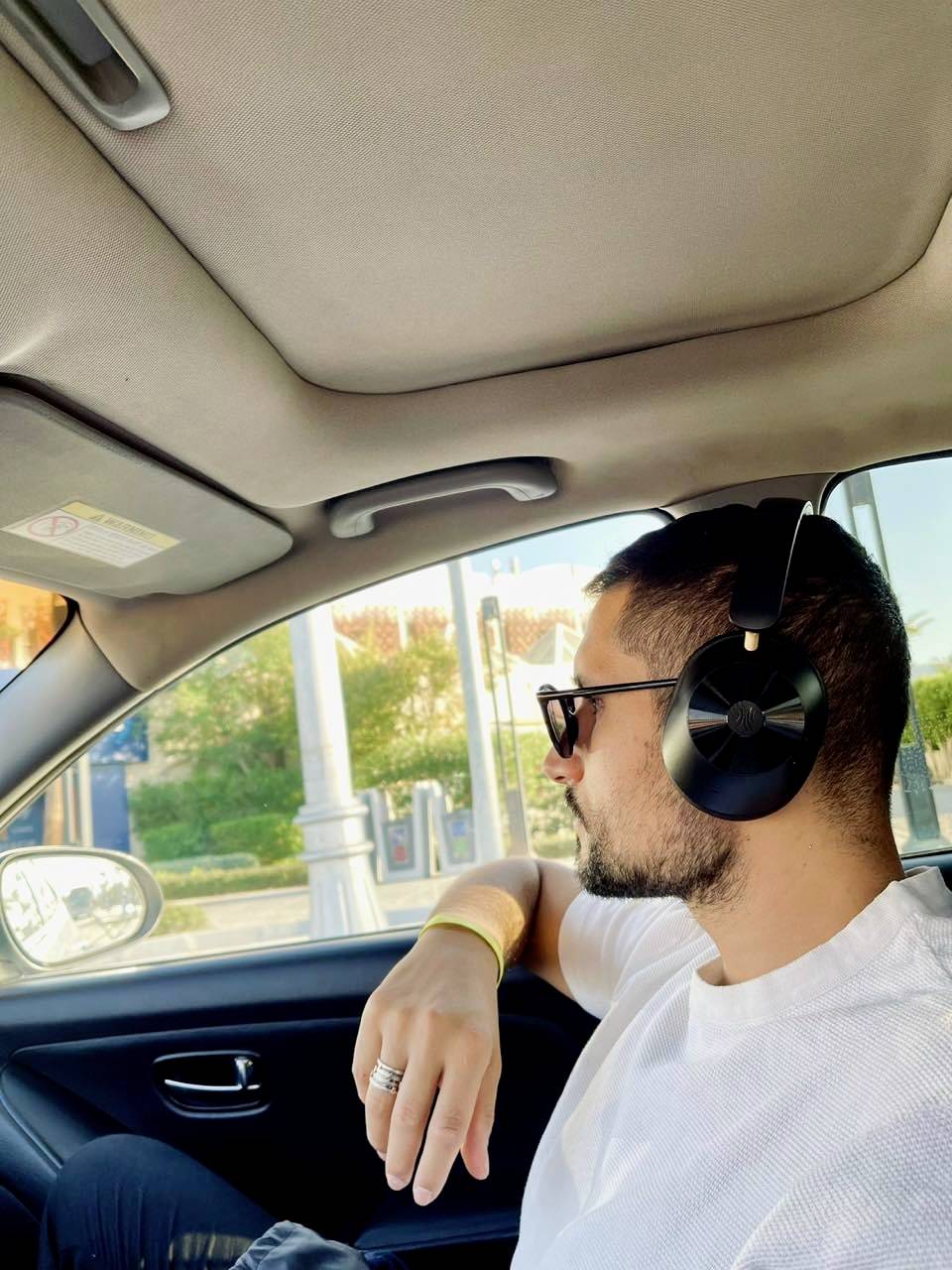 Muž se sluchátky a slunečními brýlemi sedí v autě. Dívá se z okna, relaxuje a užívá si jízdy.