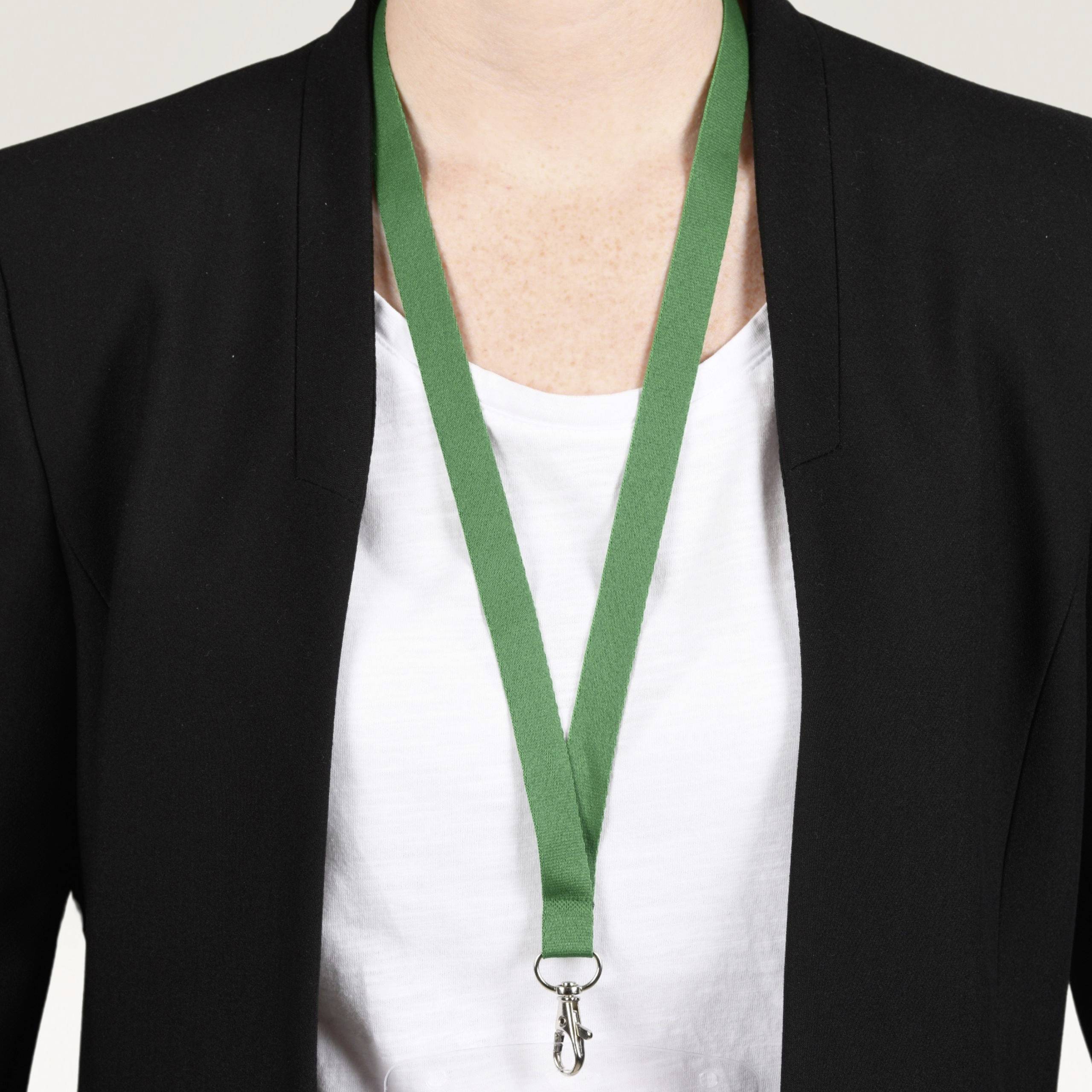 Osoba má na sobě bílou košili a černý blazer. Kolem krku má zavěšenu zelenou šňůrku s klíčem.