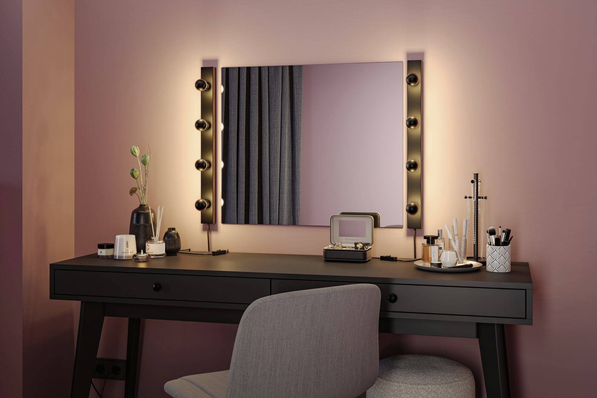 Elegantní toaletní stolek s osvětleným zrcadlem, na němž jsou rozložené různé kosmetické výrobky, a stolička v růžovém pokoji.