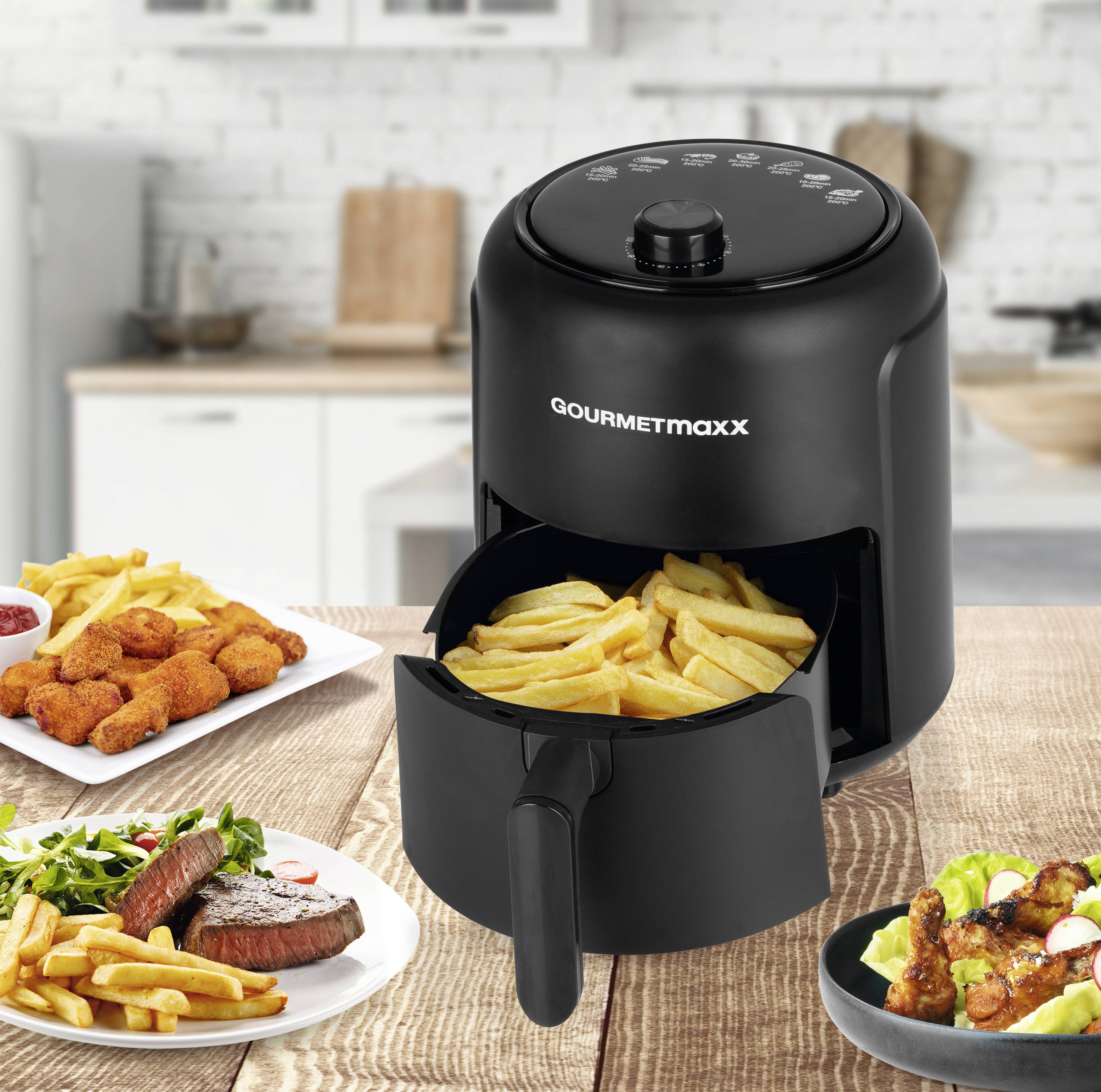 Fritéza na stole v kuchyni, naplněná hranolkami. Obklopena talíři s biftekem, hranolkami, kuřecími křidélky a dipem.