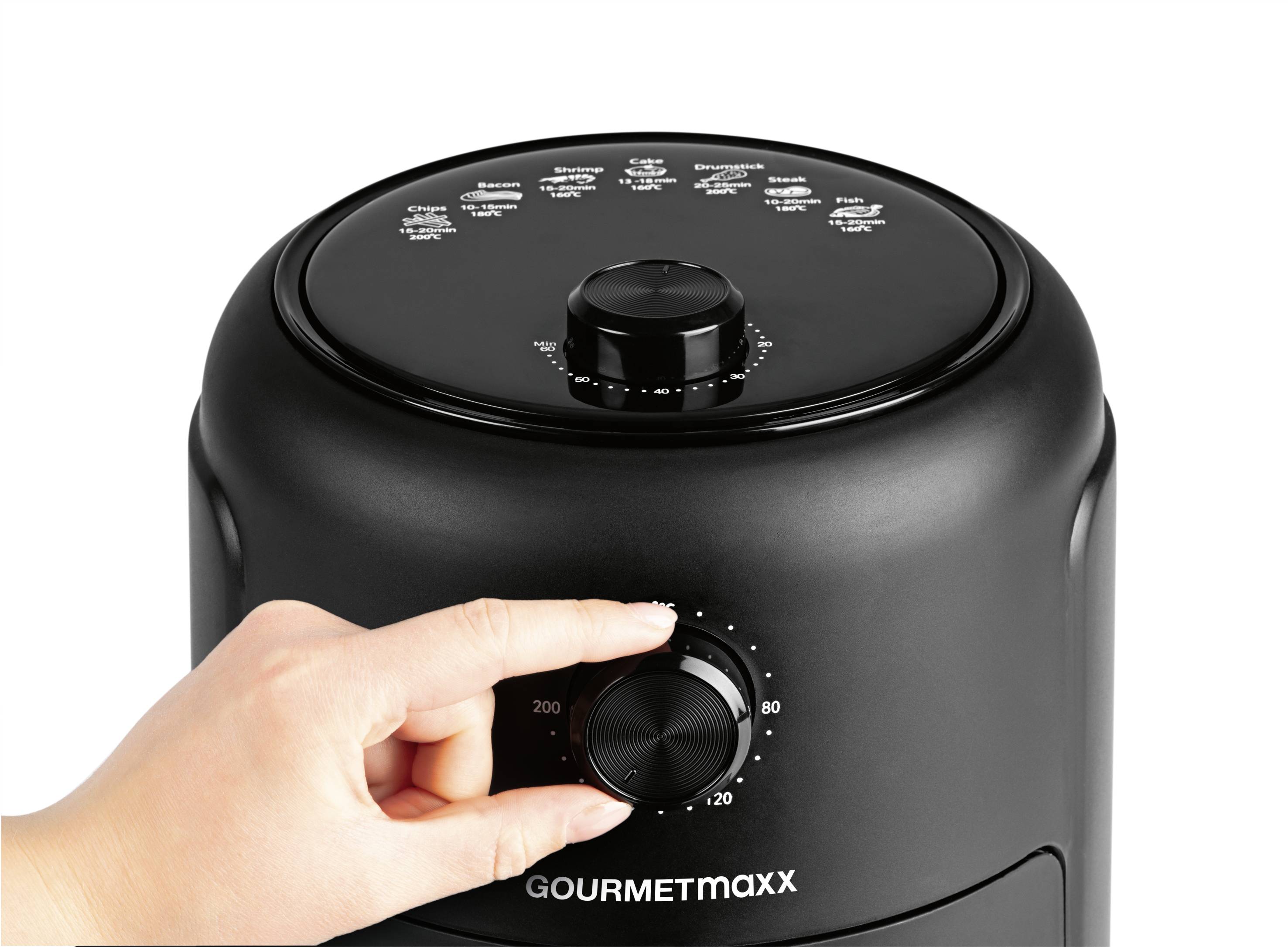 Jedna ruka otáčí regulátorem teploty černé horkovzdušné fritézy značky Gourmet Maxx. Na víku jsou vyobrazeny různé možnosti vaření.