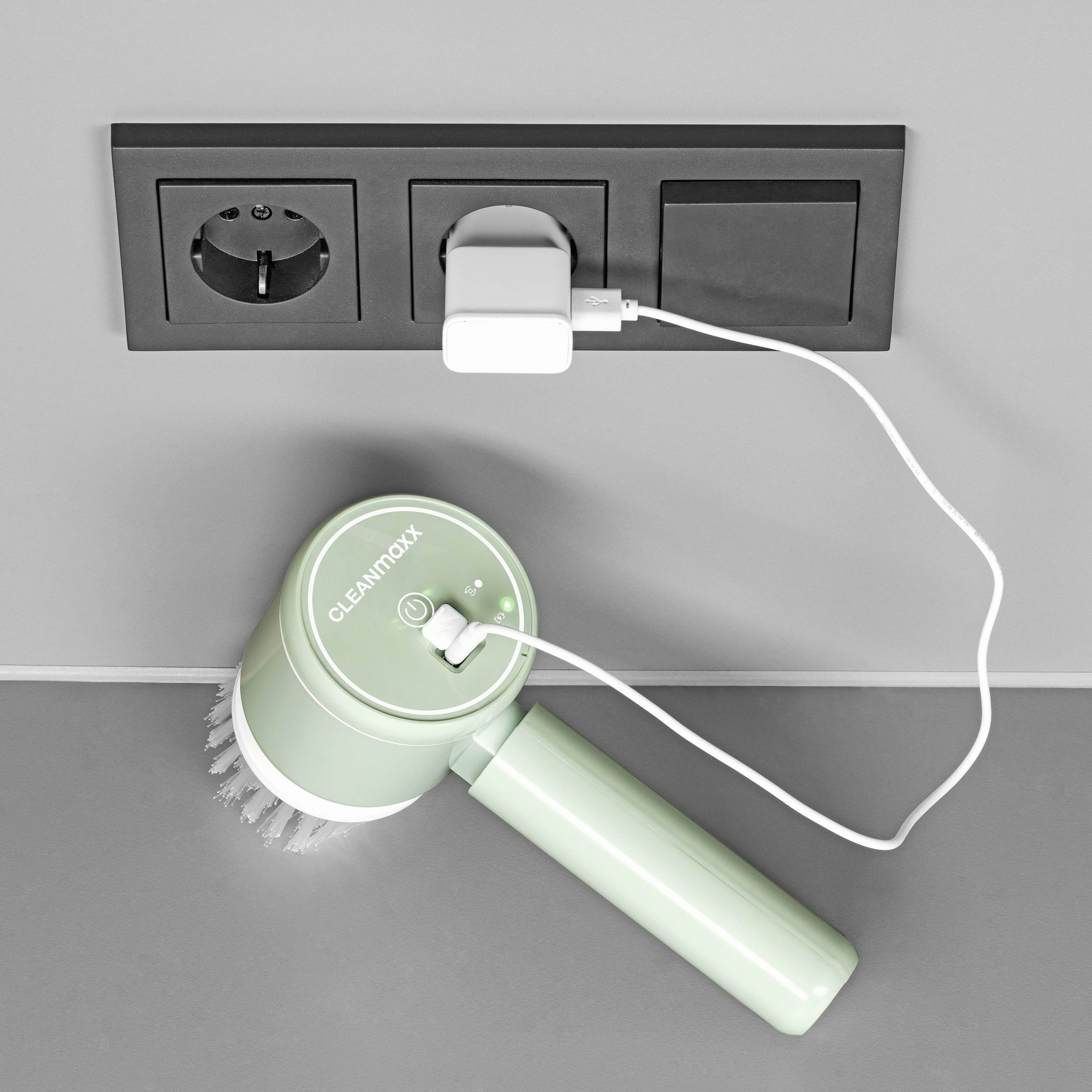 Zelené čisticí zařízení s kartáčem, které se nabíjí v elektrické zásuvce. Na zařízení svítí bílý indikátor nabíjení.