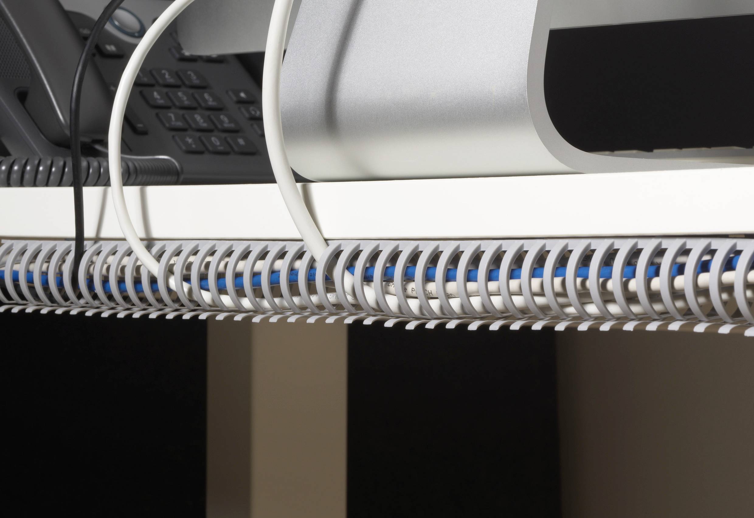 Telefonní kabel a zařízení na psacím stole, uspořádané pomocí kabelových úchytek.