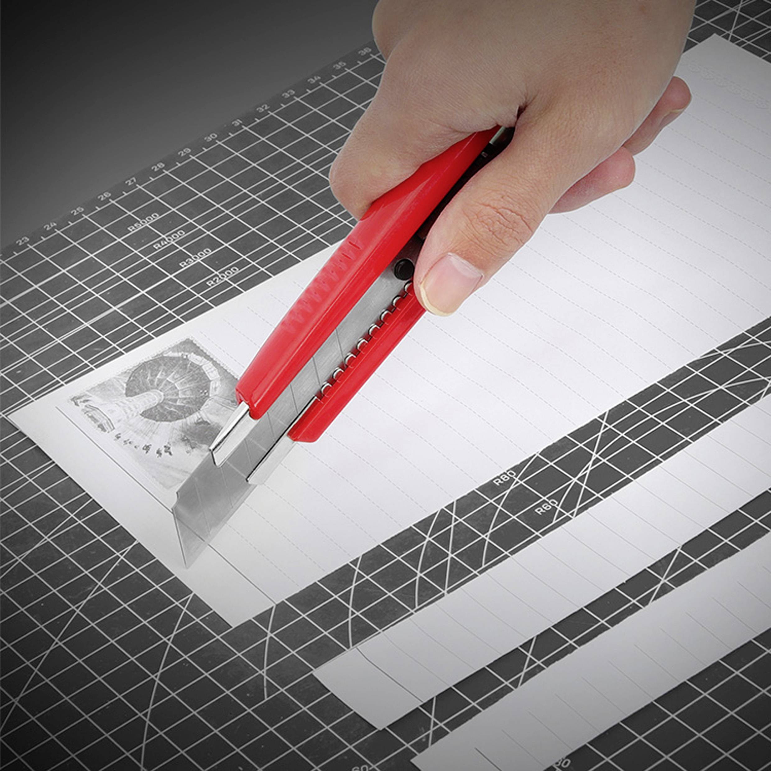 Ruka řeže pruhované bílé papíry červeným řezacím nožem na řezací podložce.