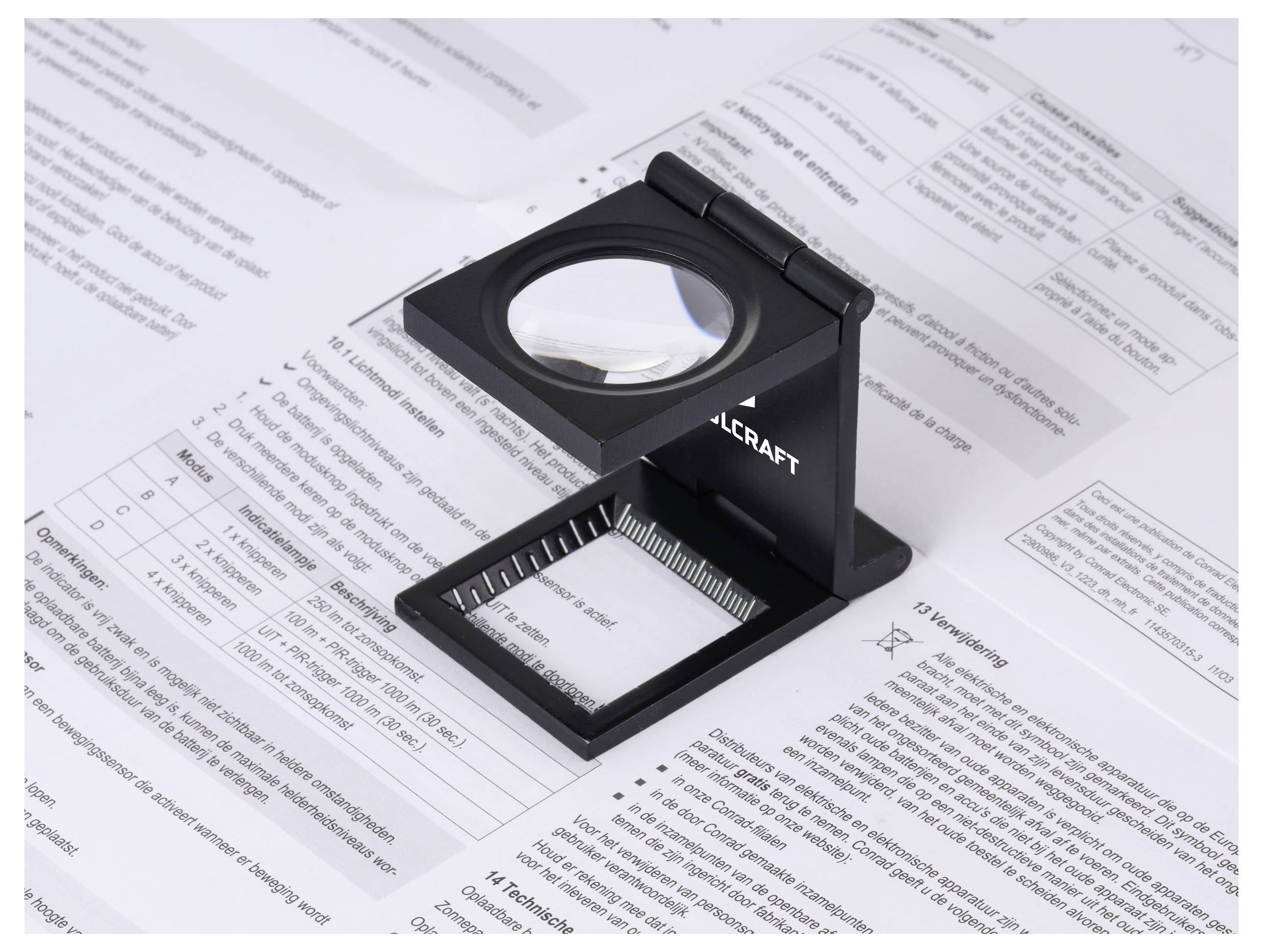 Lupa s měřicí stupnicí leží na technickém dokumentu plném tabulkových dat a textu, což naznačuje detailní analýzu.