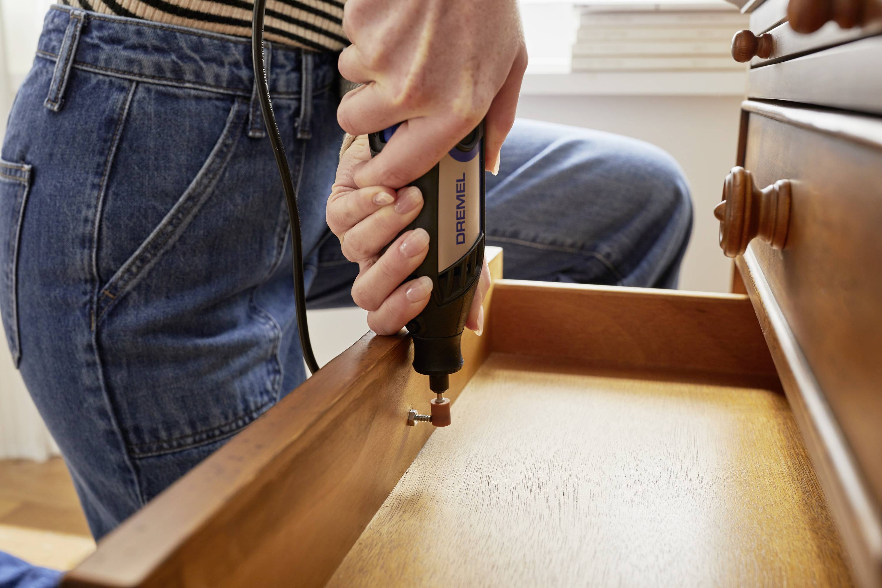 Osoba opracovává dřevěnou zásuvku ručním nástrojem v domácím prostředí.