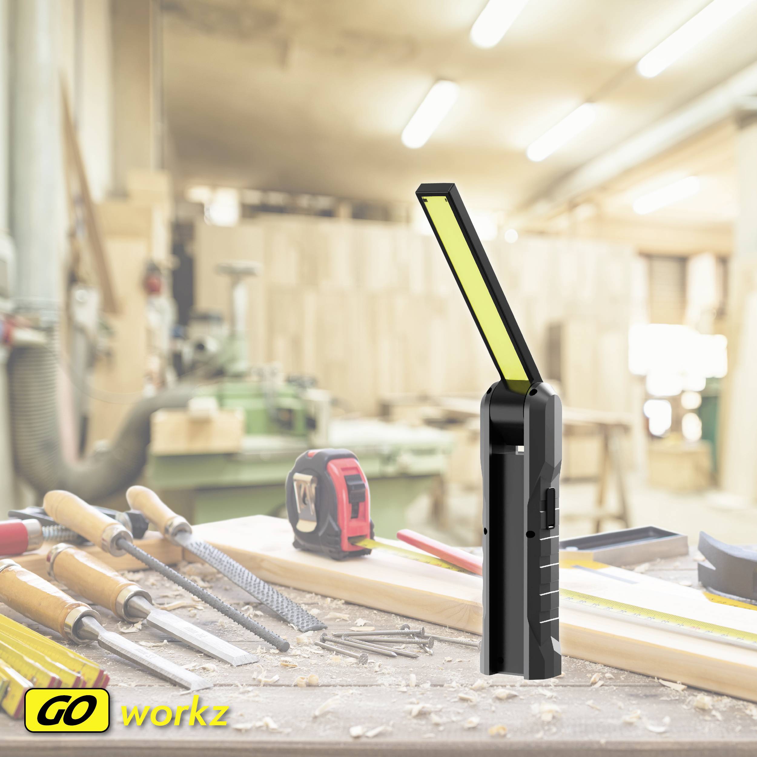 V dílně plné ručního nářadí stojí černá sklopná pracovní lampa v popředí. Vlevo dole je logo 'GO workz'.