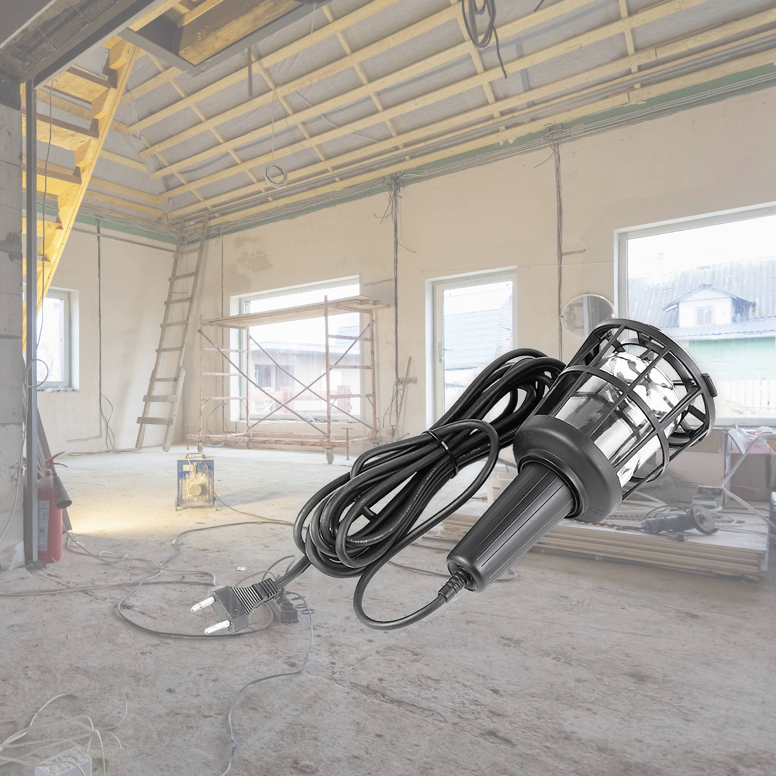 Prázdný stavební prostor s otevřenými okny a volným kabelem ležícím na zemi. Přenosná stavební lampa je připravena k použití.