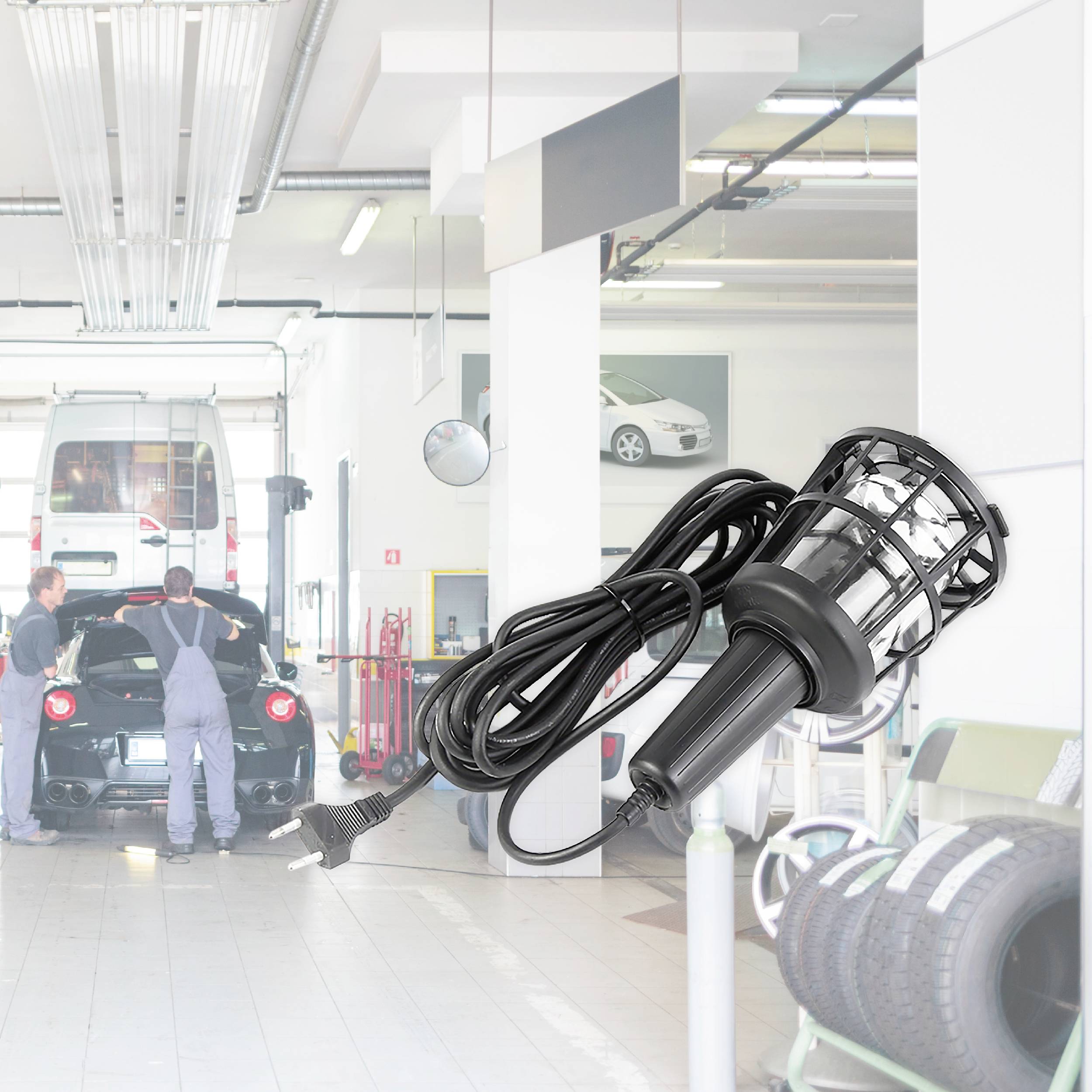 Mechanici pracují na červeném autě v dílně, kde jsou zřetelně viditelné pneumatiky a lampa, zatímco bílé auto stojí na zdviži.