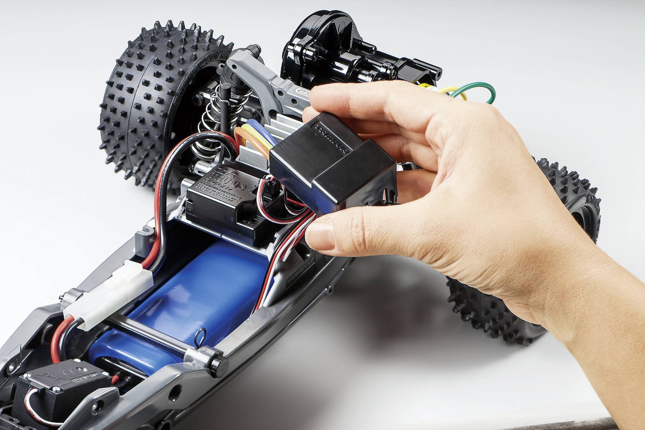 Ruka provádí jemné seřízení součástky v dálkově ovládaném automobilu. Viditelné kabely a komponenty. Zaměření na technické jemné doladění.