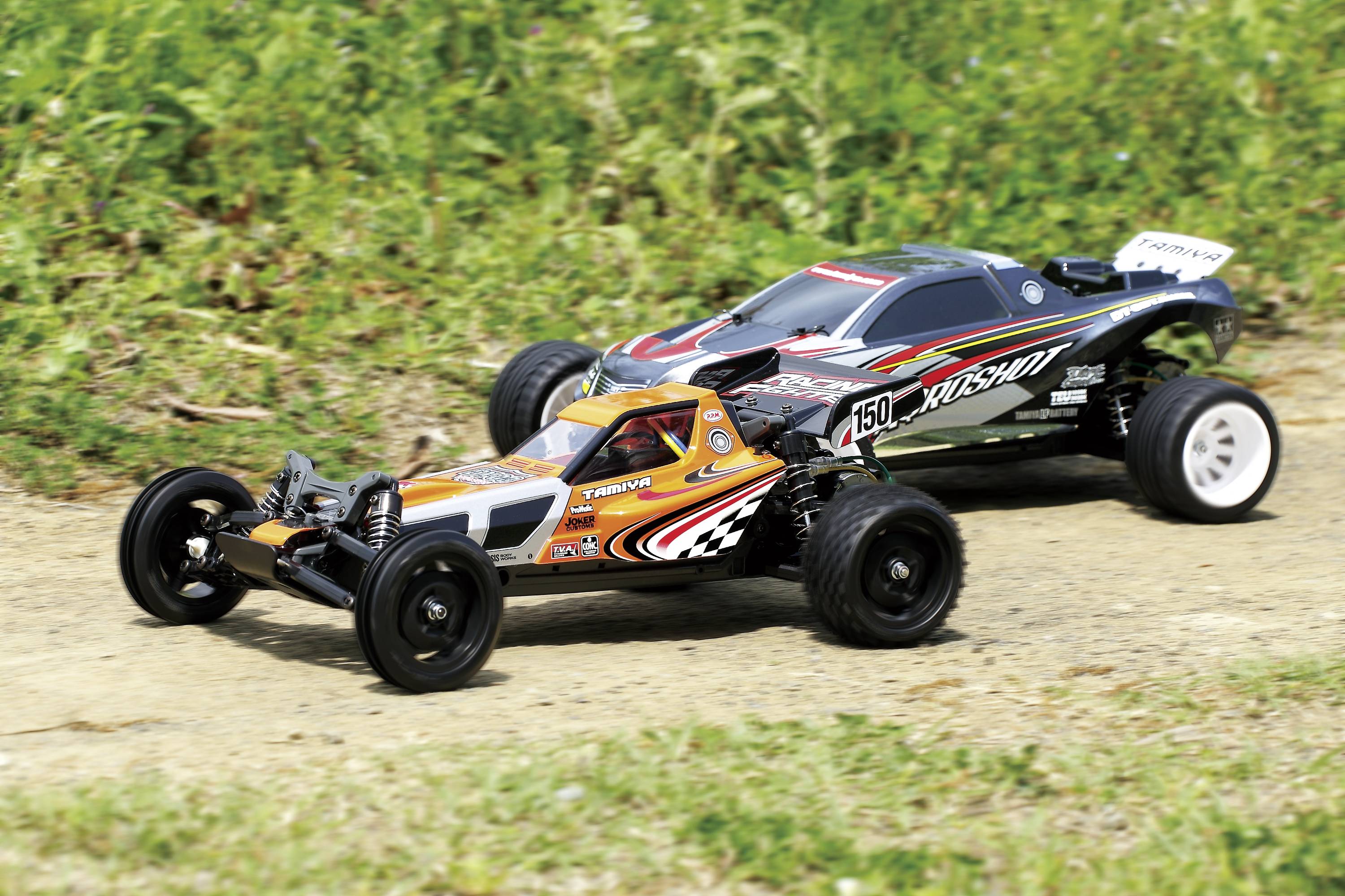 Dva dálkově ovládané vozy na venkovní závodní dráze, oba s nápadnými designovými prvky. Přední vůz má oranžové a černé vzory.