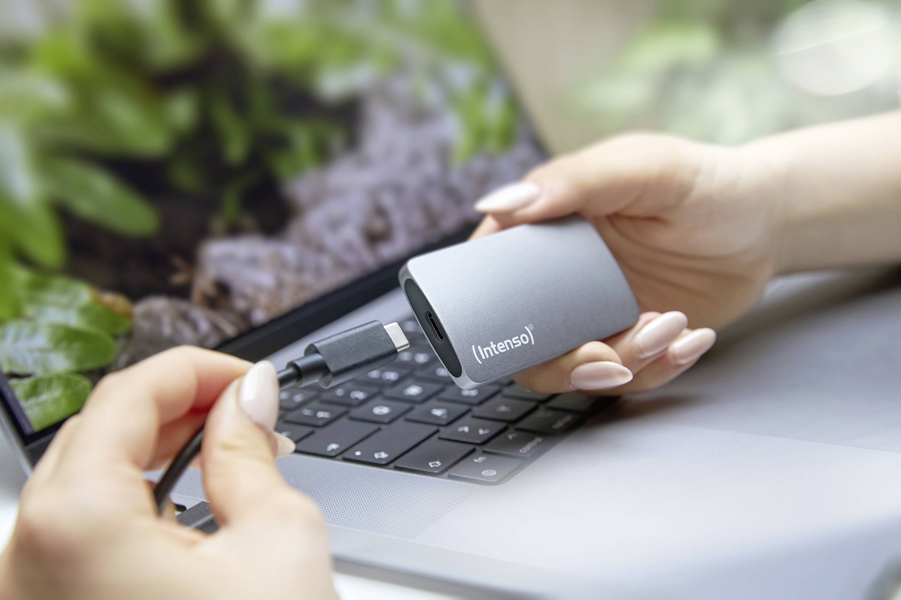 Osoba drží externí pevný disk před notebookem a chystá se jej připojit pomocí USB kabelu.