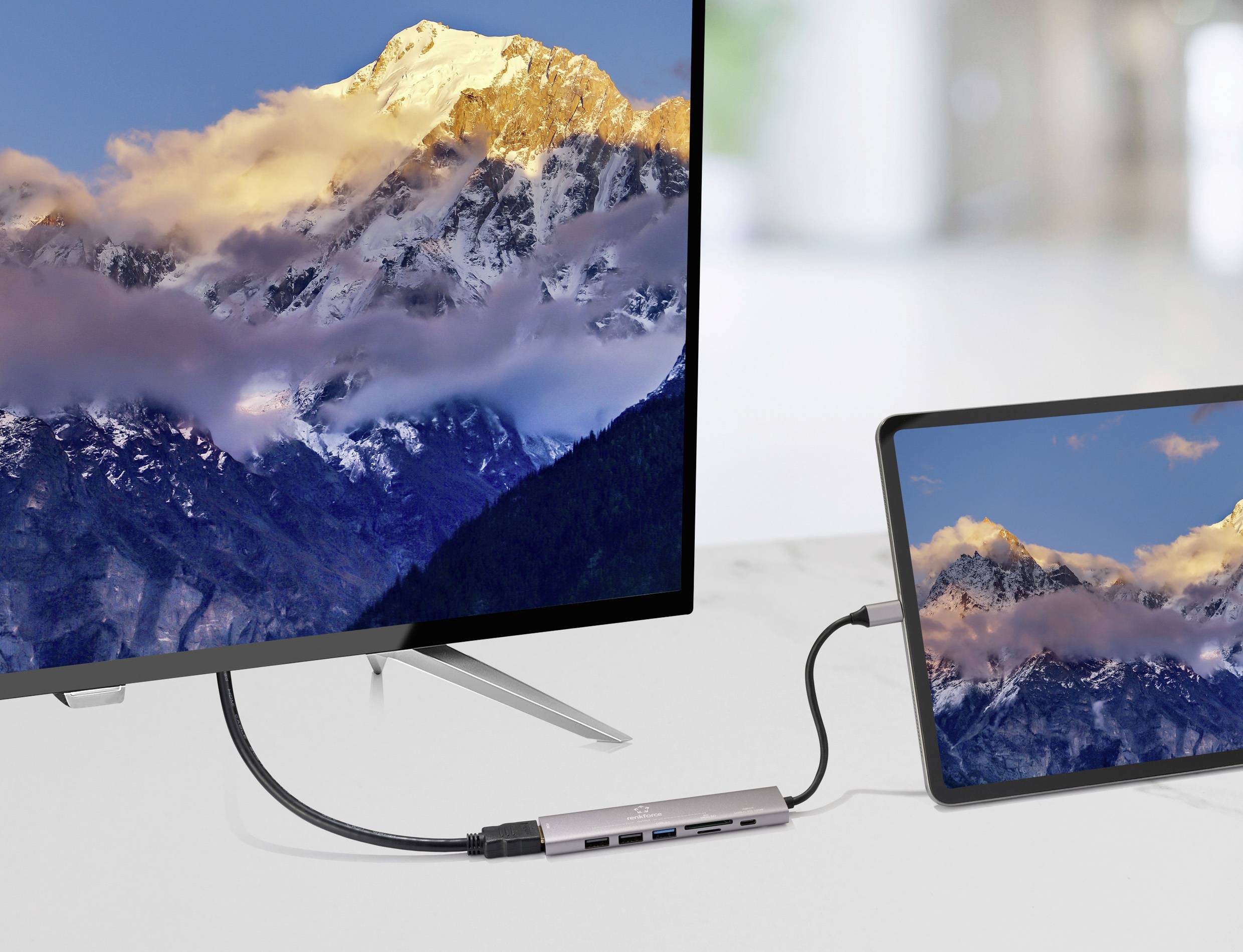 Laptop připojený k monitoru zobrazuje stejnou horskou scenérii se západem slunce, což ukazuje konektivitu zařízení a zrcadlení obrazovky.