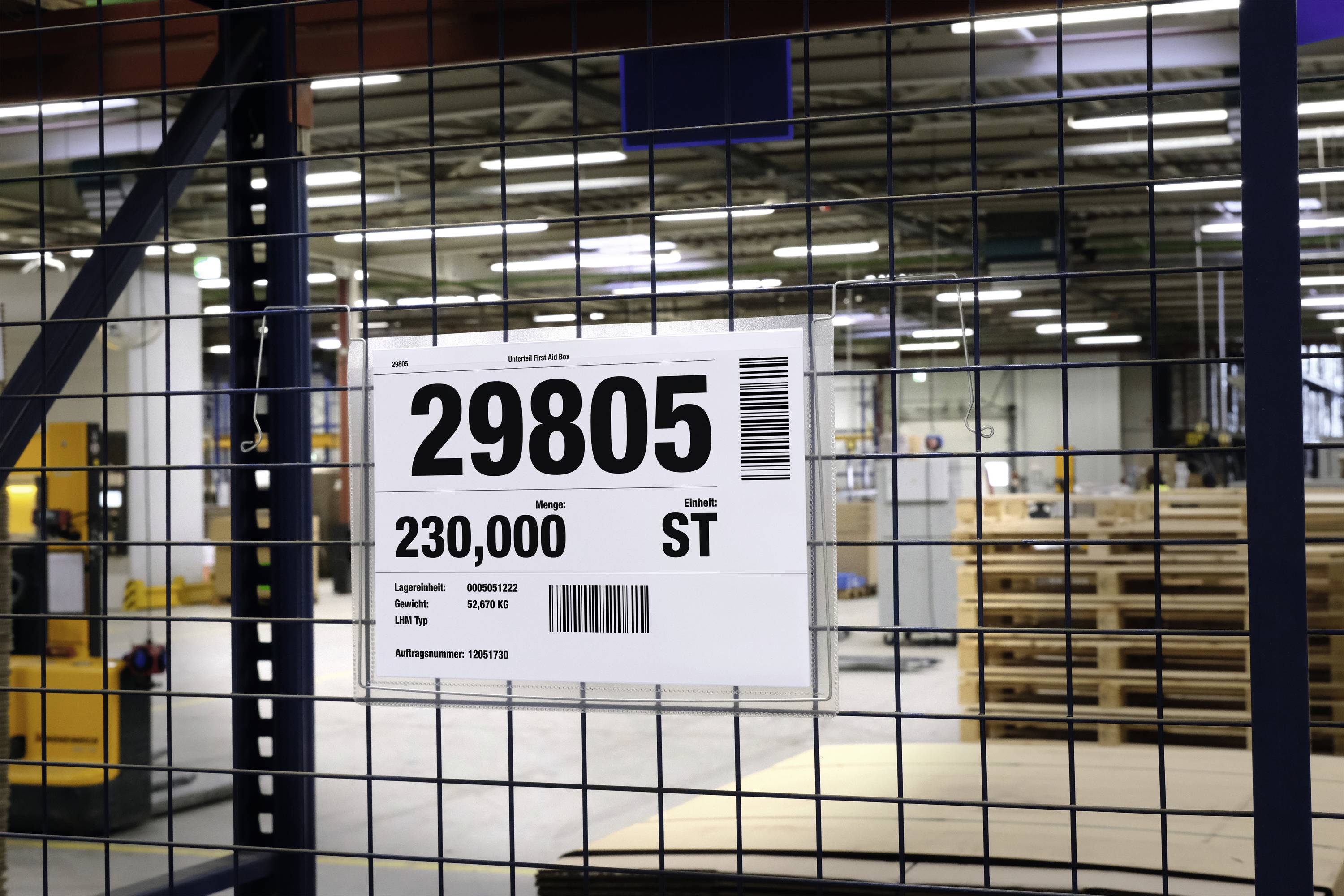 Štítek s nápisem '29805 ST', namontovaný na regálu skladu, ukazuje množství 230.000. V pozadí je viditelná skladová hala.