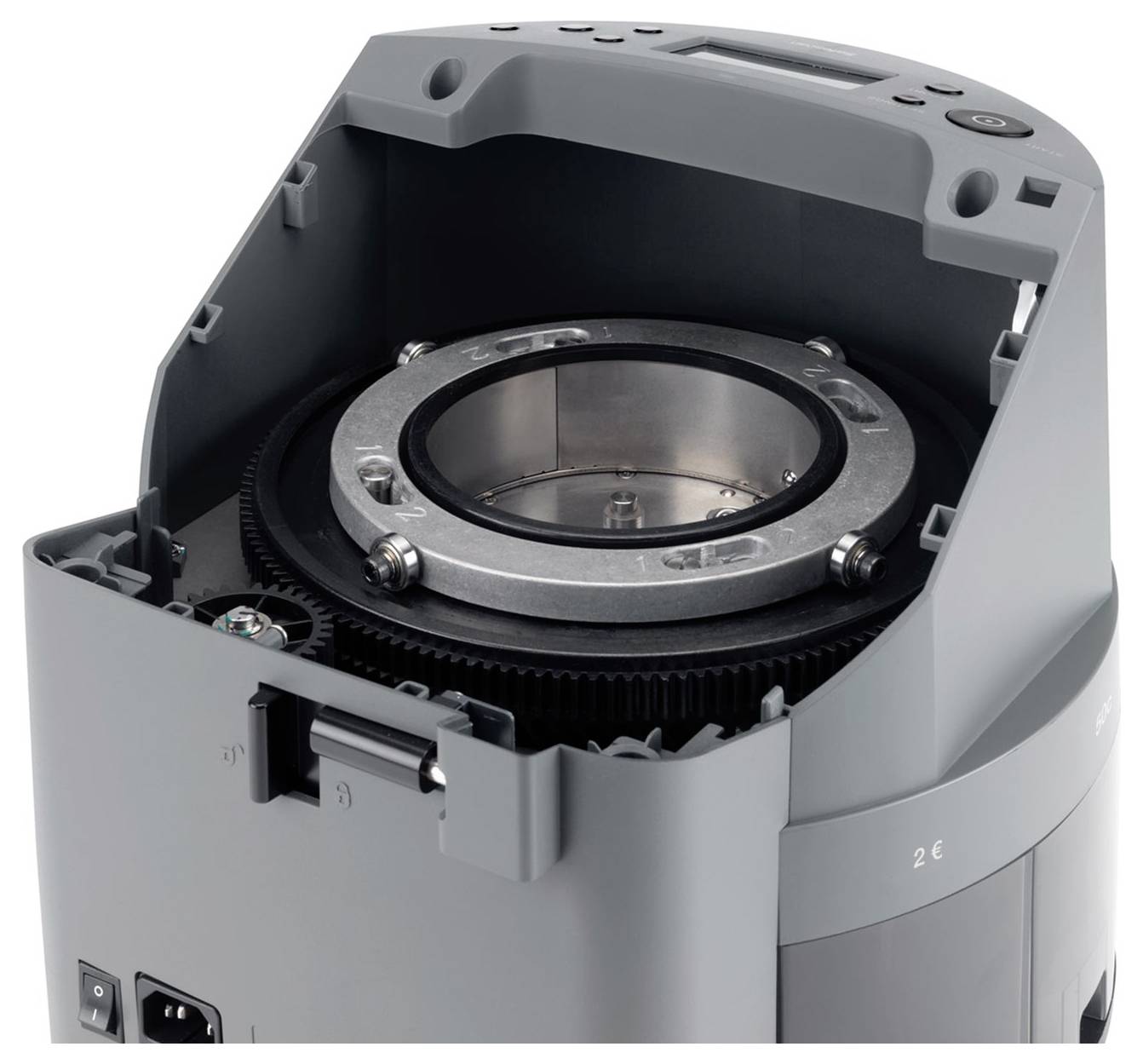 Šedé průmyslové zařízení s otevřeným krytem, viditelným kovovým válcem a ozubenými koly, pravděpodobně technická součástka.