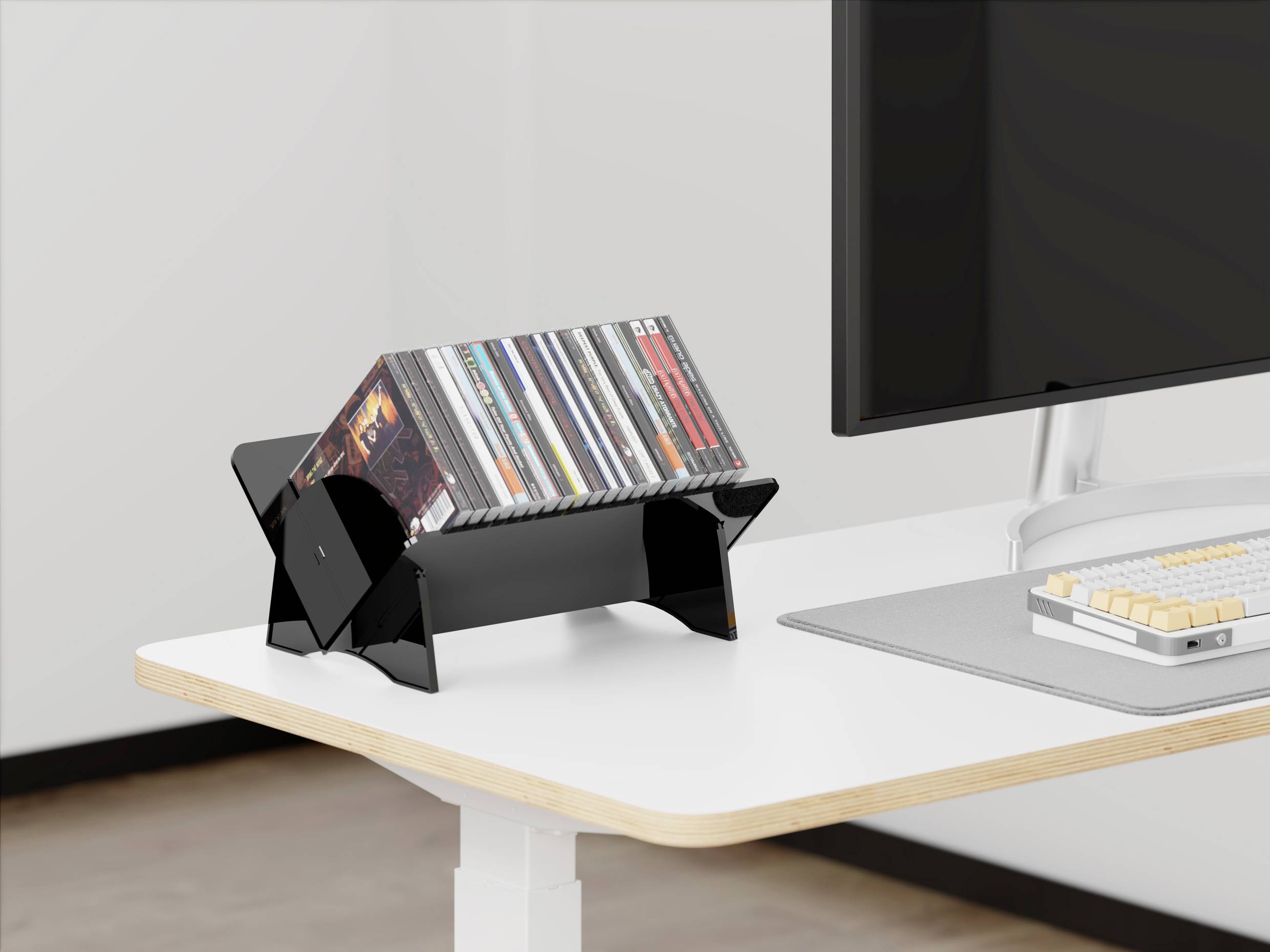 Moderní kancelářský stůl s monitorem a klávesnicí. Černý stojan na CD přidává pracovnímu prostoru nádech retro stylu.