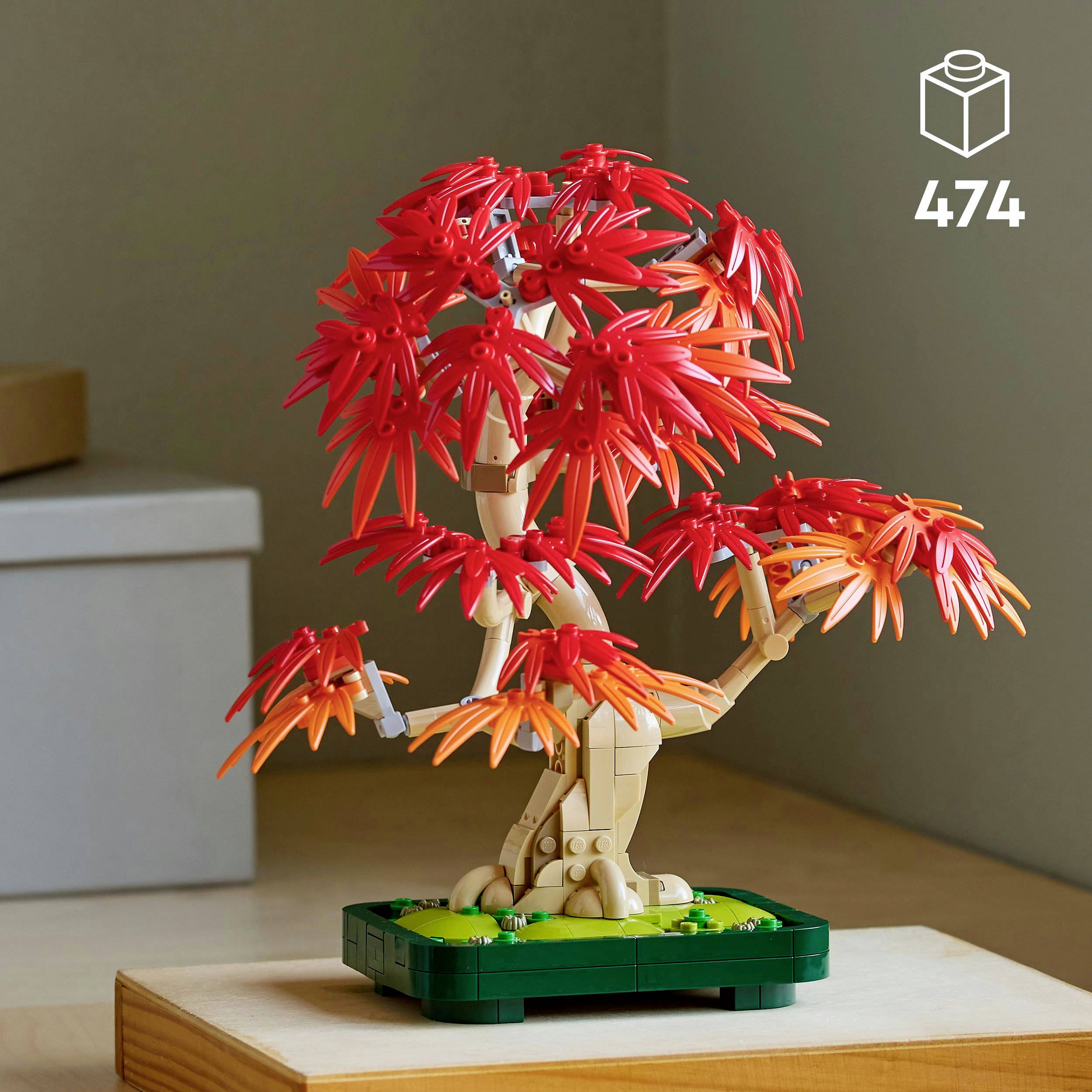 LEGO bonsai strom s červenými listy stojí na dřevěném stole, v pozadí jsou vidět krabice.
