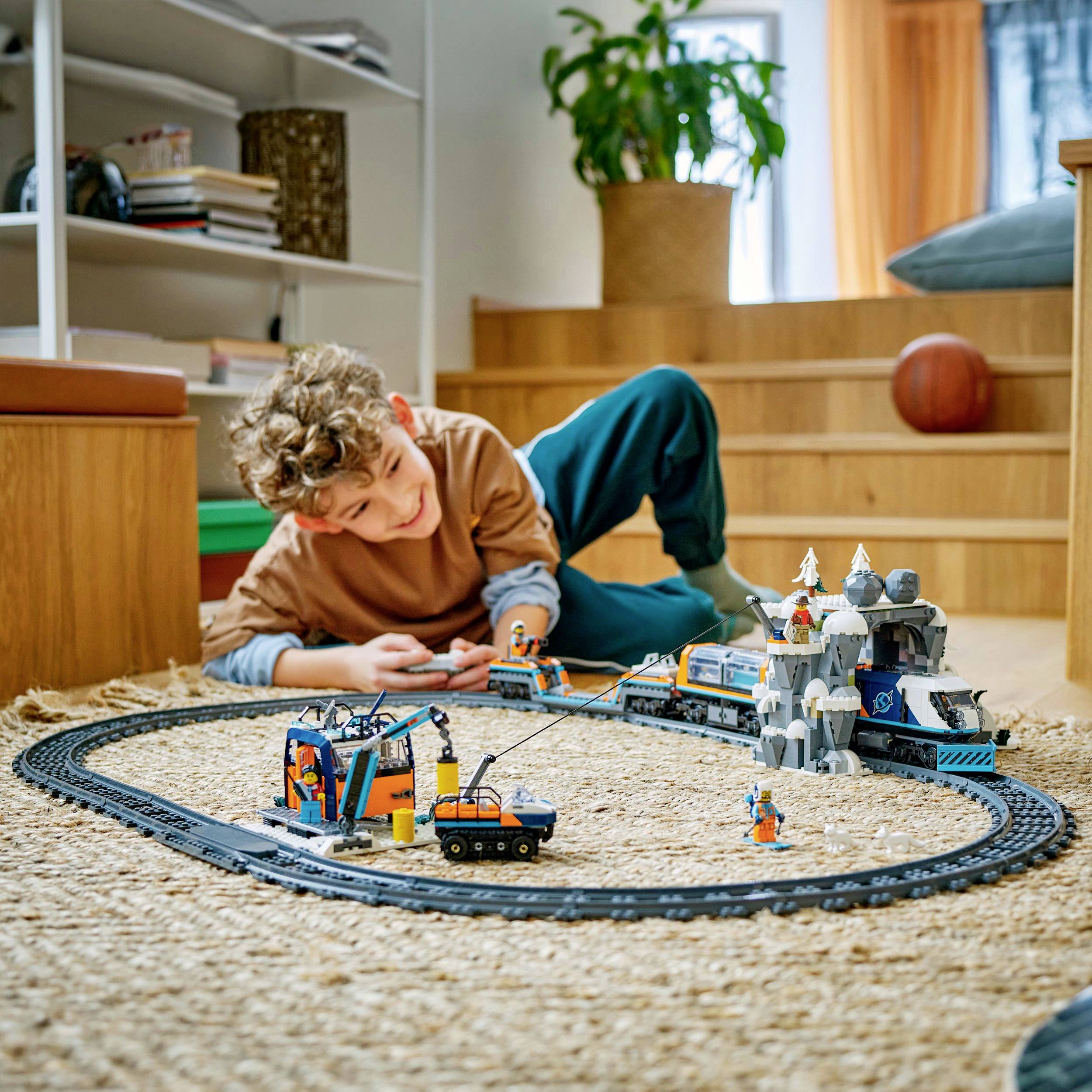 Dítě si hraje s elektrickou hračkářskou železnicí na kulatém koberci v obývacím pokoji.