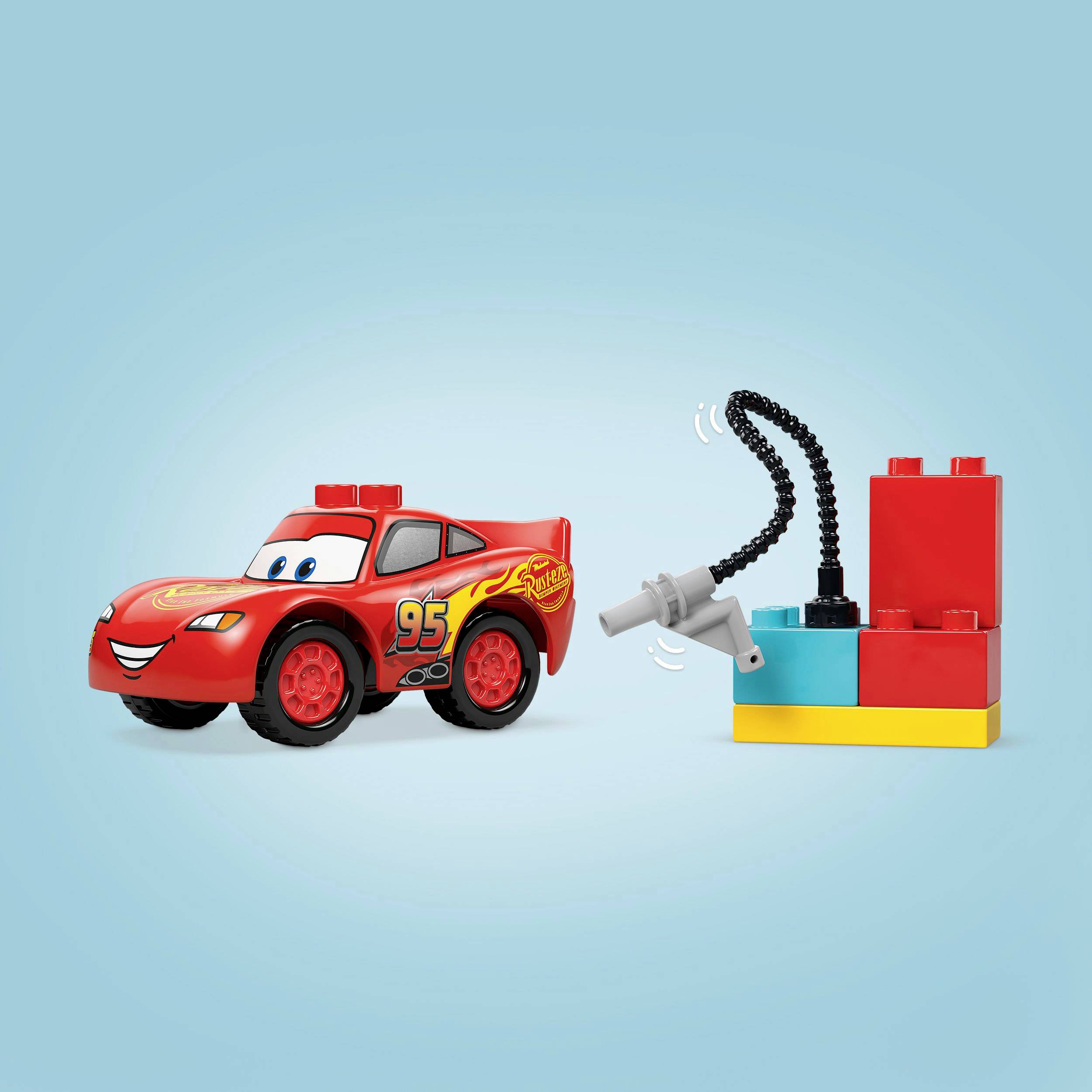 Červené hračkářské auto s číslem 95 a motivem plamenů je zobrazeno vedle barevné Lego čerpací stanice.