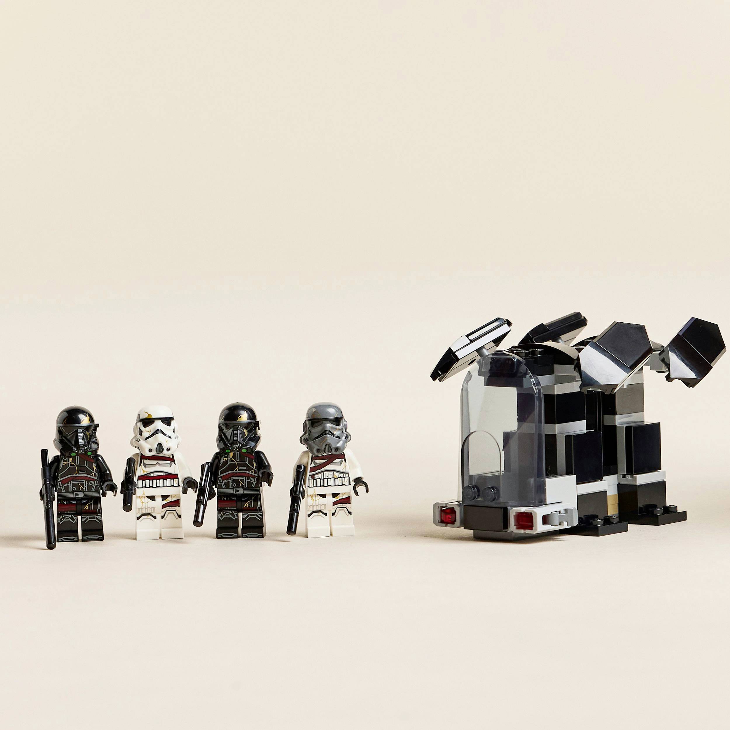 Čtyři Lego figurky v černých a bílých zbrojích stojí vedle malého, černého modelu vesmírné lodi na světlém pozadí.