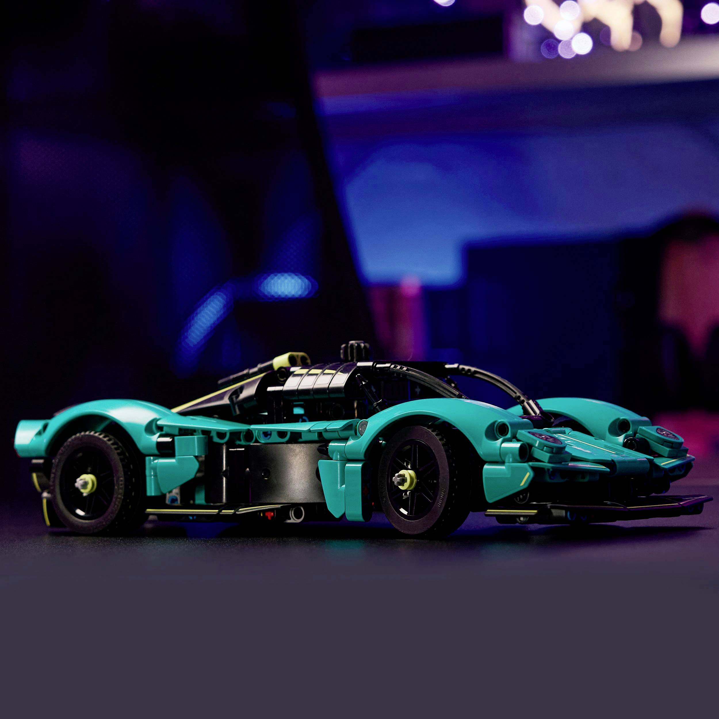 Tyrkysové hračkářské sportovní auto v popředí, před pozadím s rozmazaným modrým a fialovým světlem.