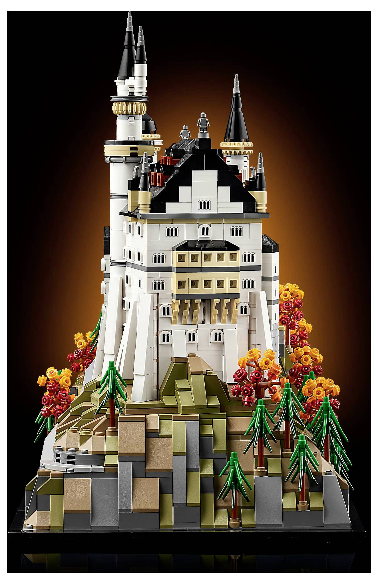 Detailní LEGO model hradu s vysokými věžemi a barevnou vegetací, umístěný na skalnaté základně, s oranžovým zářícím pozadím.