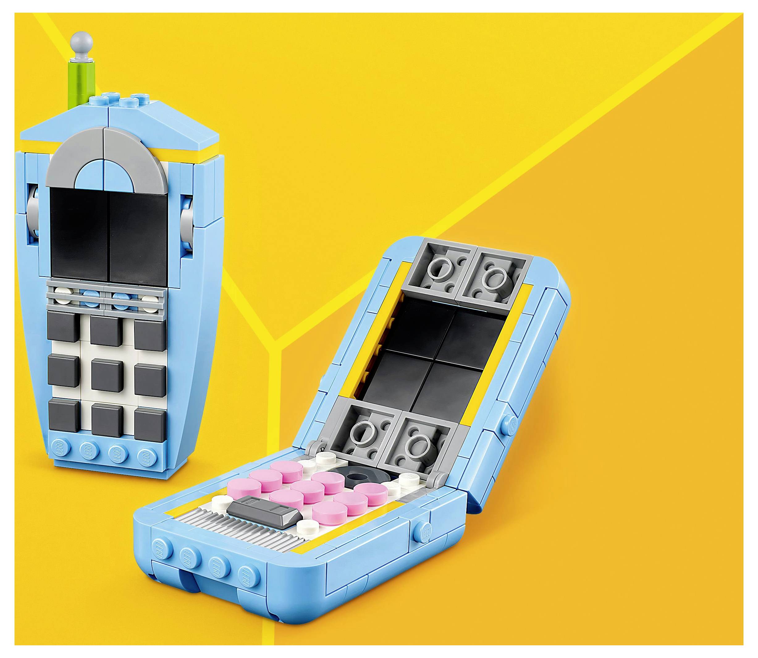 Dva mobilní telefony postavené z kostek LEGO na žlutém pozadí: zavřený skládací telefon s růžovými tlačítky a vzpřímený telefon s černou obrazovkou.