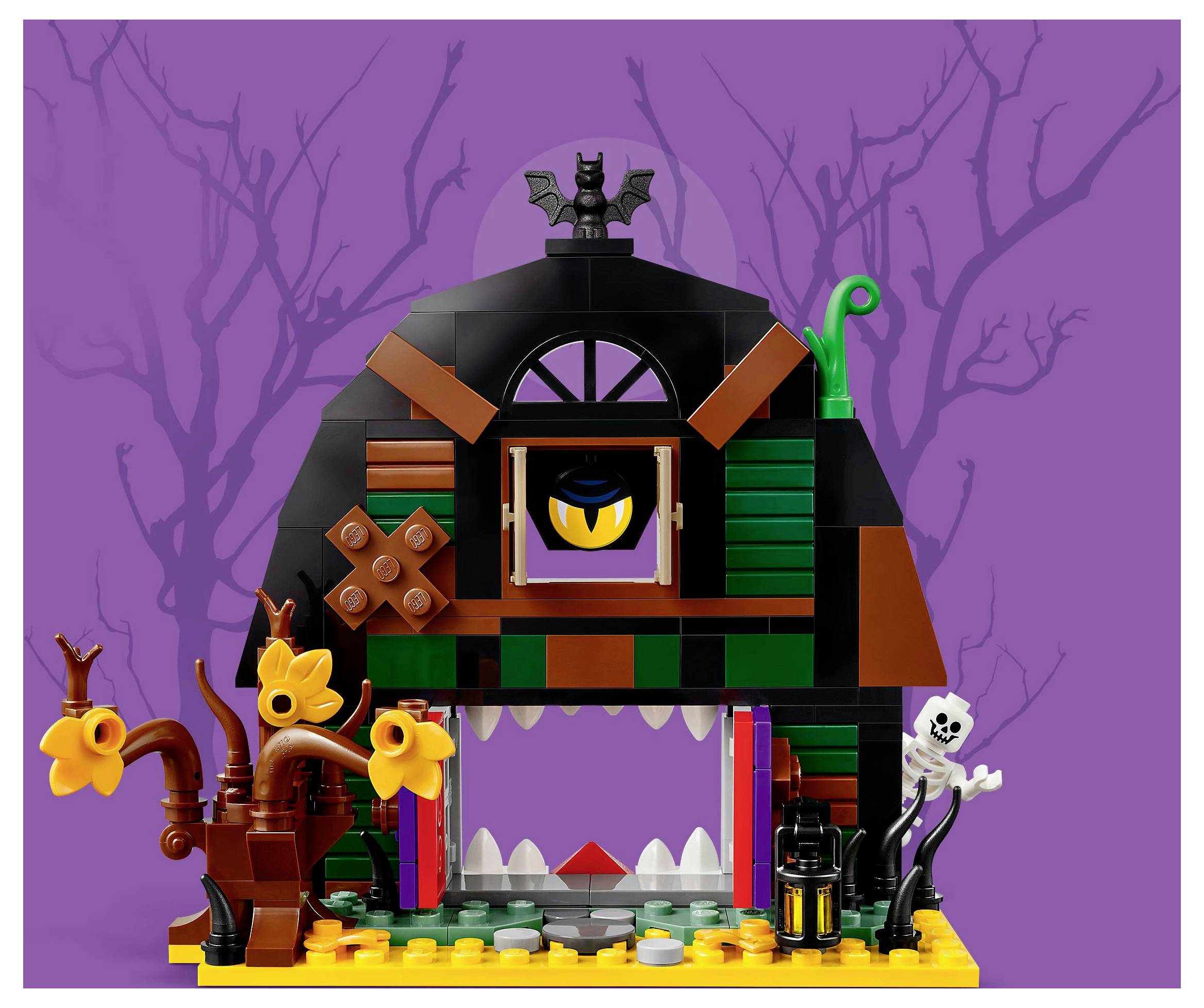 Barevná sada LEGO strašidelného domu zobrazuje monster s vyvalenýma očima, jehož dveře mají tvar úst, obklopené strašidelnými stromy a kostrou.