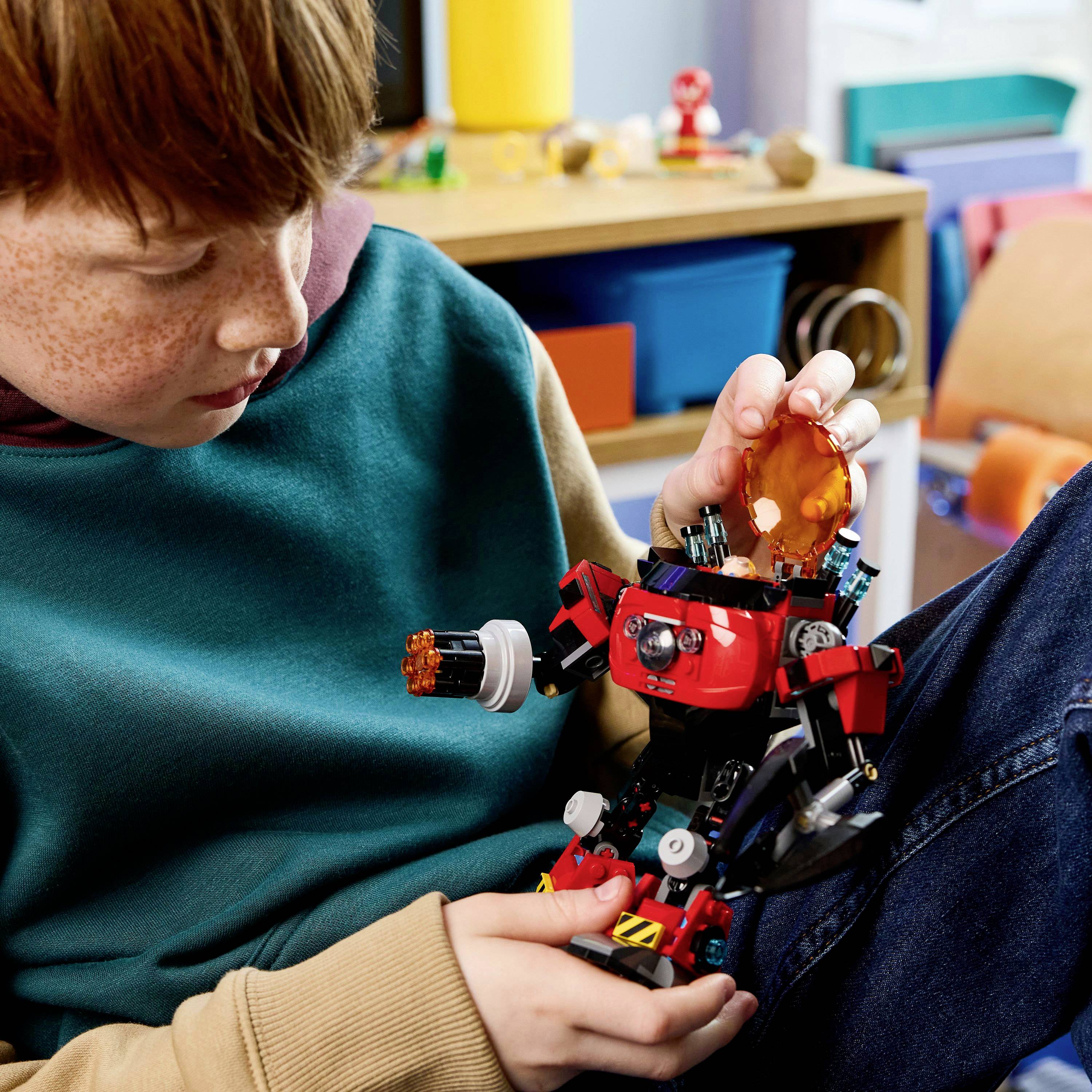 Dítě sedící na gauči montuje robotickou hračku se světle červenými díly v útulné, barevné místnosti. Dítě je soustředěné a plně zaujané.