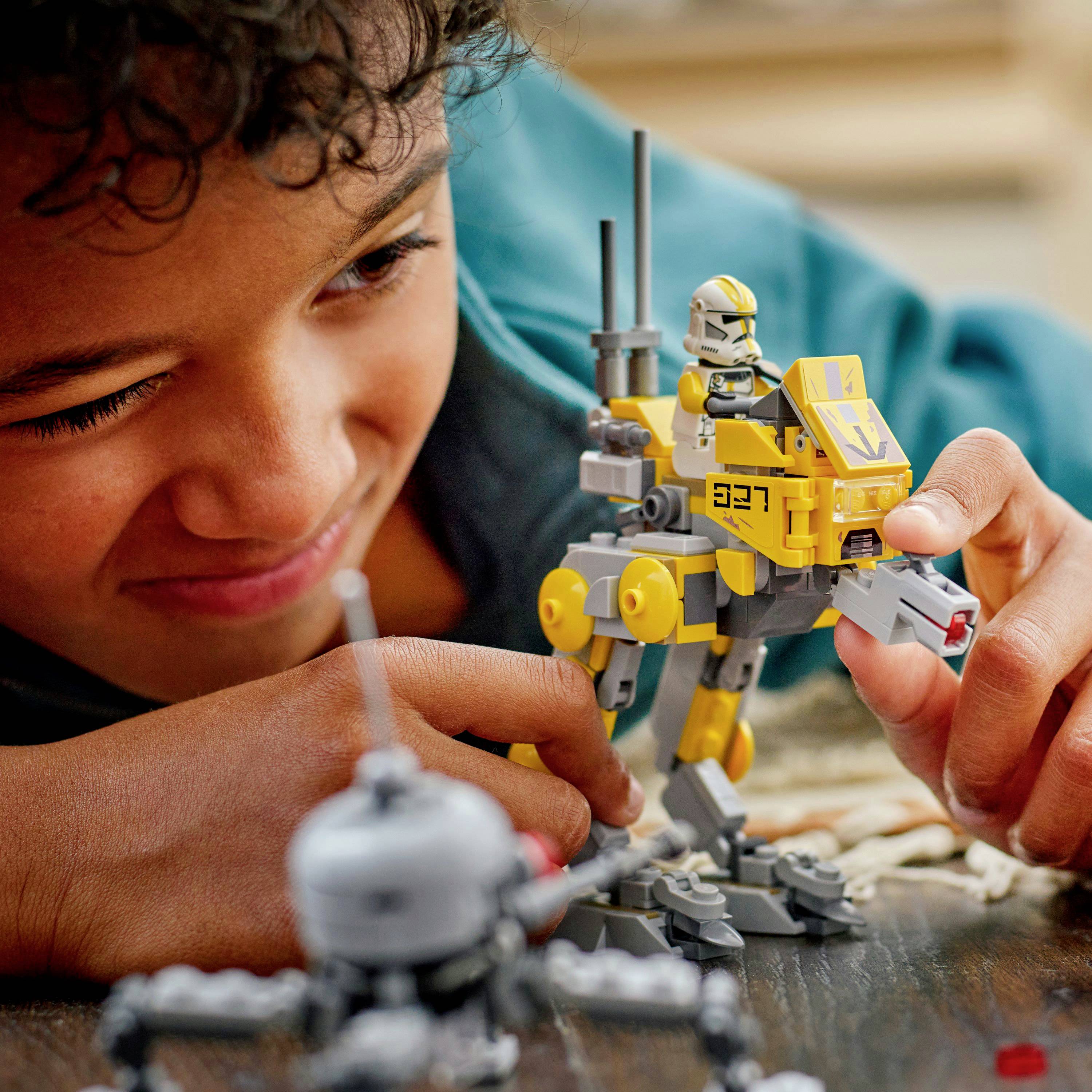 Dítě se usmívá a hraje si s žluto-šedou robotickou hračkou, soustředěně zkoumá její mechanické části. V rozostřeném popředí jsou další hračky.