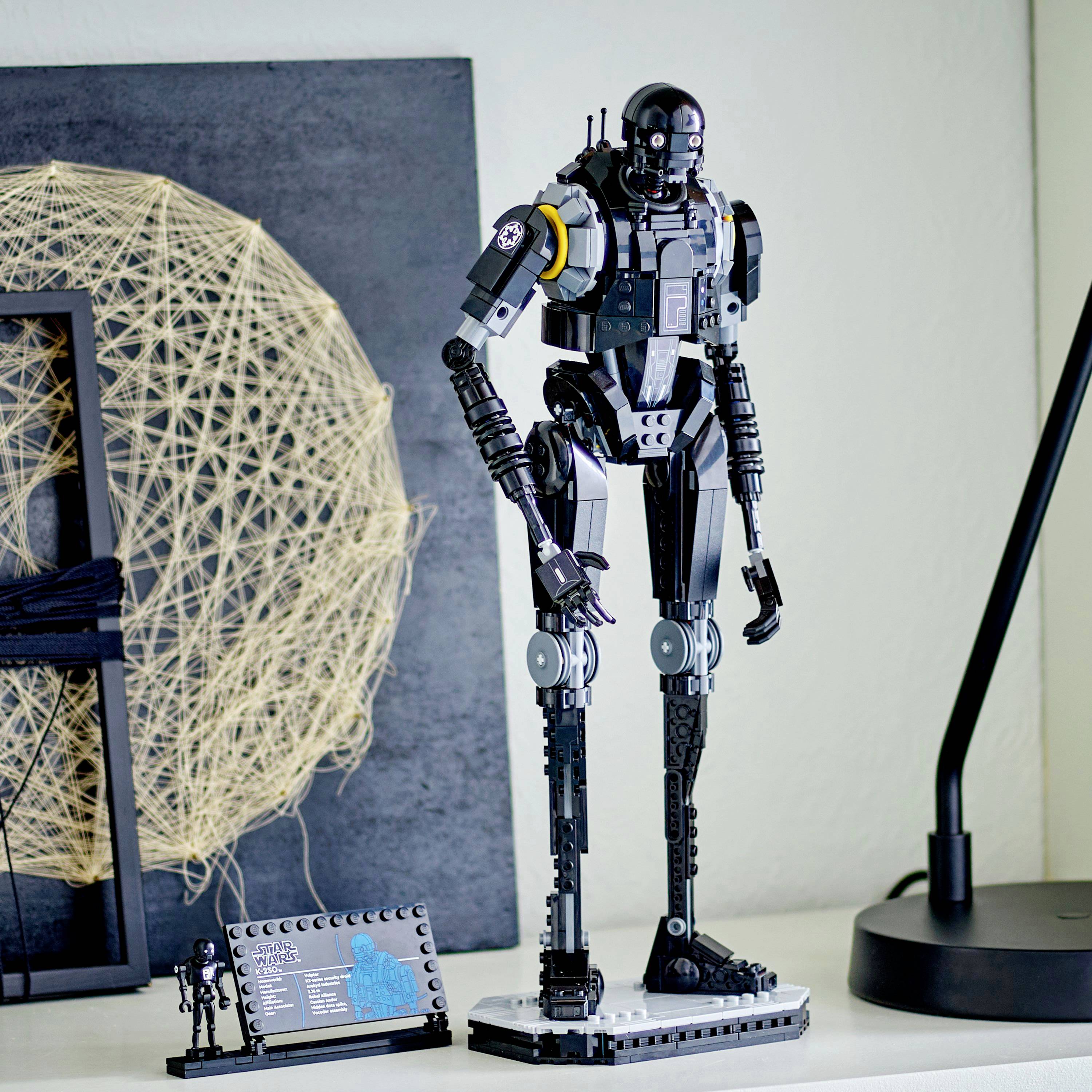 Detailní model humanoidního robota stojí na polici, obklopený moderním interiérovým designem. Robot vykazuje složité mechanické detaily.