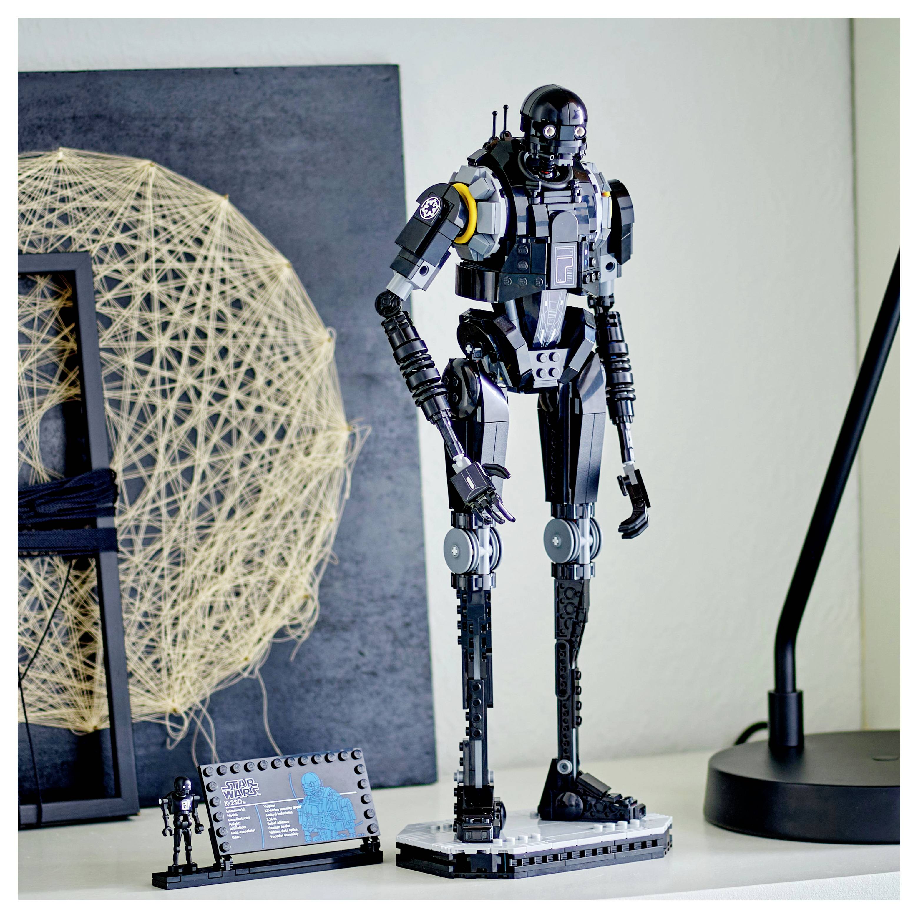 Detailní LEGO model vysokého černého robota s propracovanými designovými prvky, umístěný na polici vedle dekorativního umění.