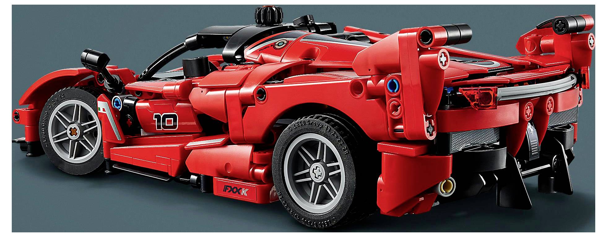 Červený model sportovního autíčka s detailními prvky jako jsou kola, spoiler a číslo startovního čísla '10', umístěný na tmavém pozadí.