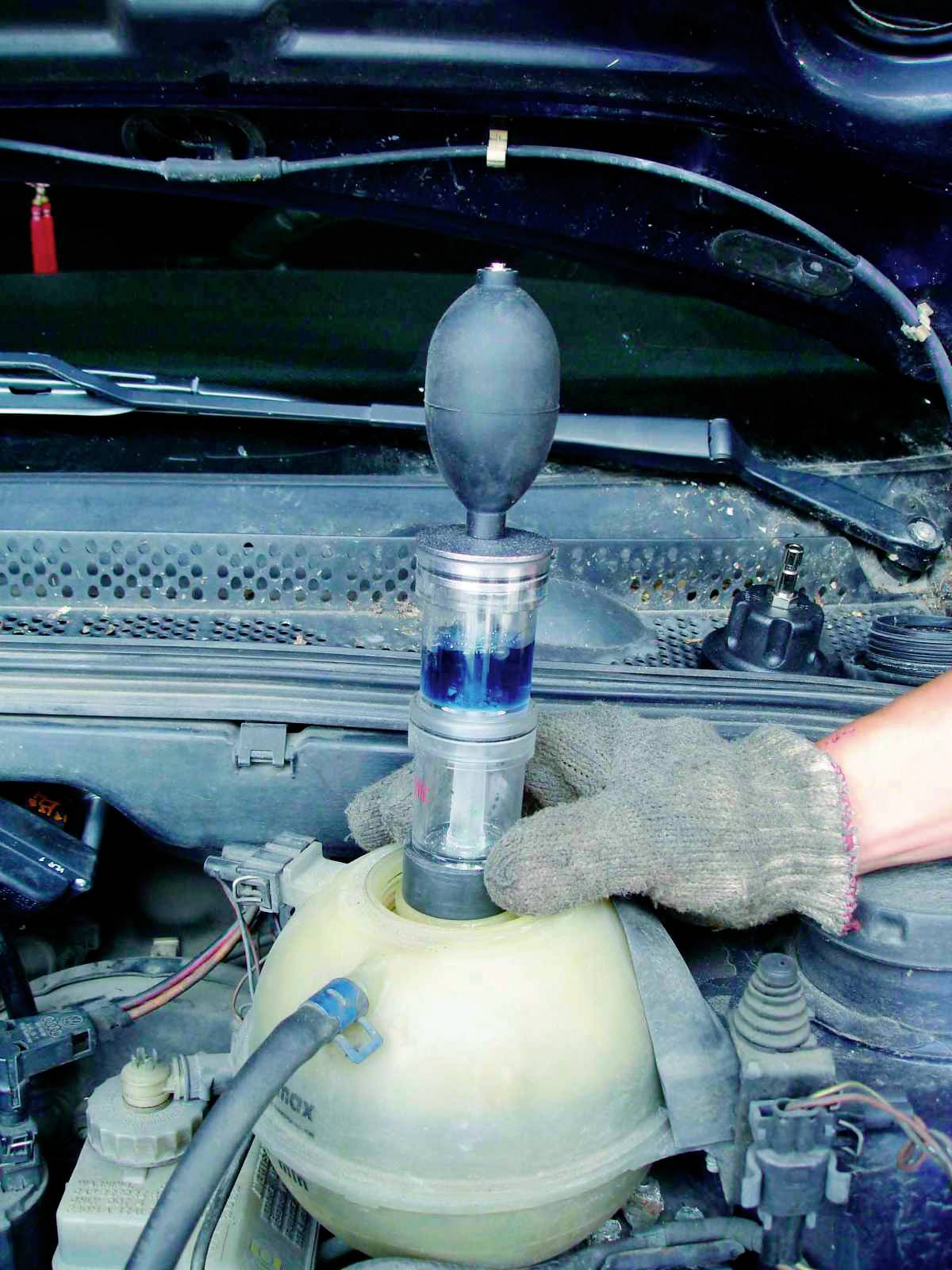 Osoba kontroluje chladicí kapalinu automobilu pomocí testeru chladicí kapaliny, který je zaveden do nádržky.