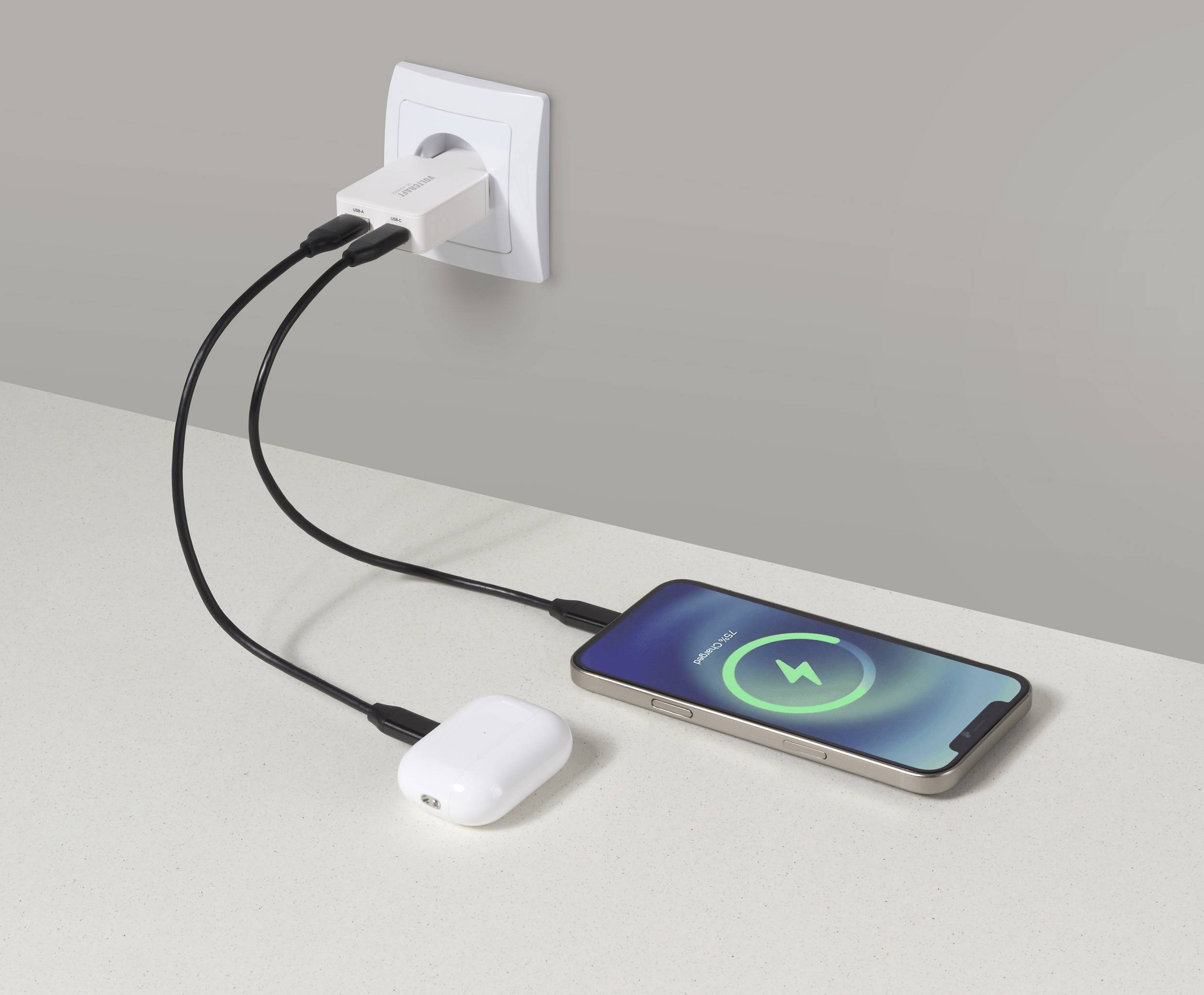 Telefon a bezdrátová sluchátka nabíjející se na pultu pomocí duálního USB síťového adaptéru; na displeji telefonu je zobrazován symbol nabíjení.